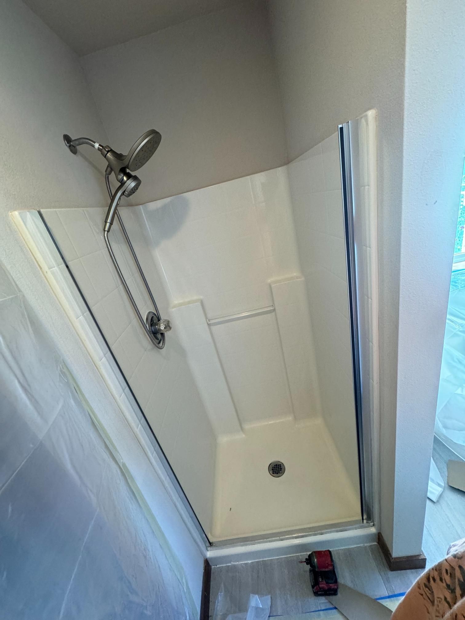 White corner shower with showerhead and handheld sprayer, framed by a sliding glass door.