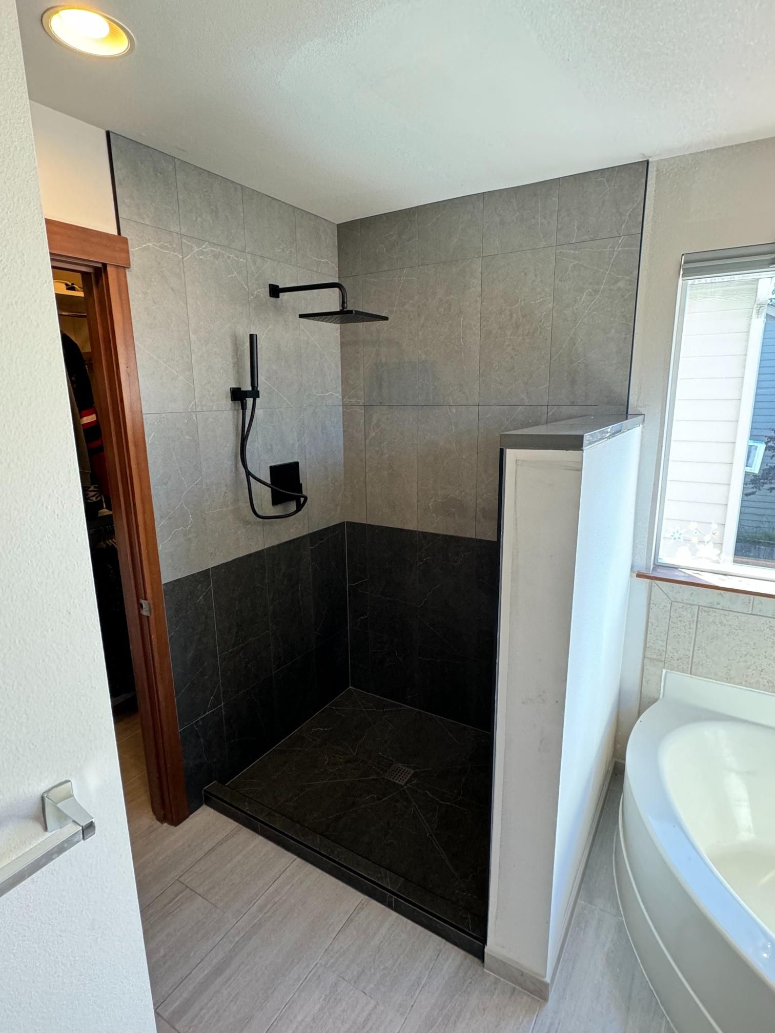 Modern shower with gray and black tile, black fixtures, and white wall.