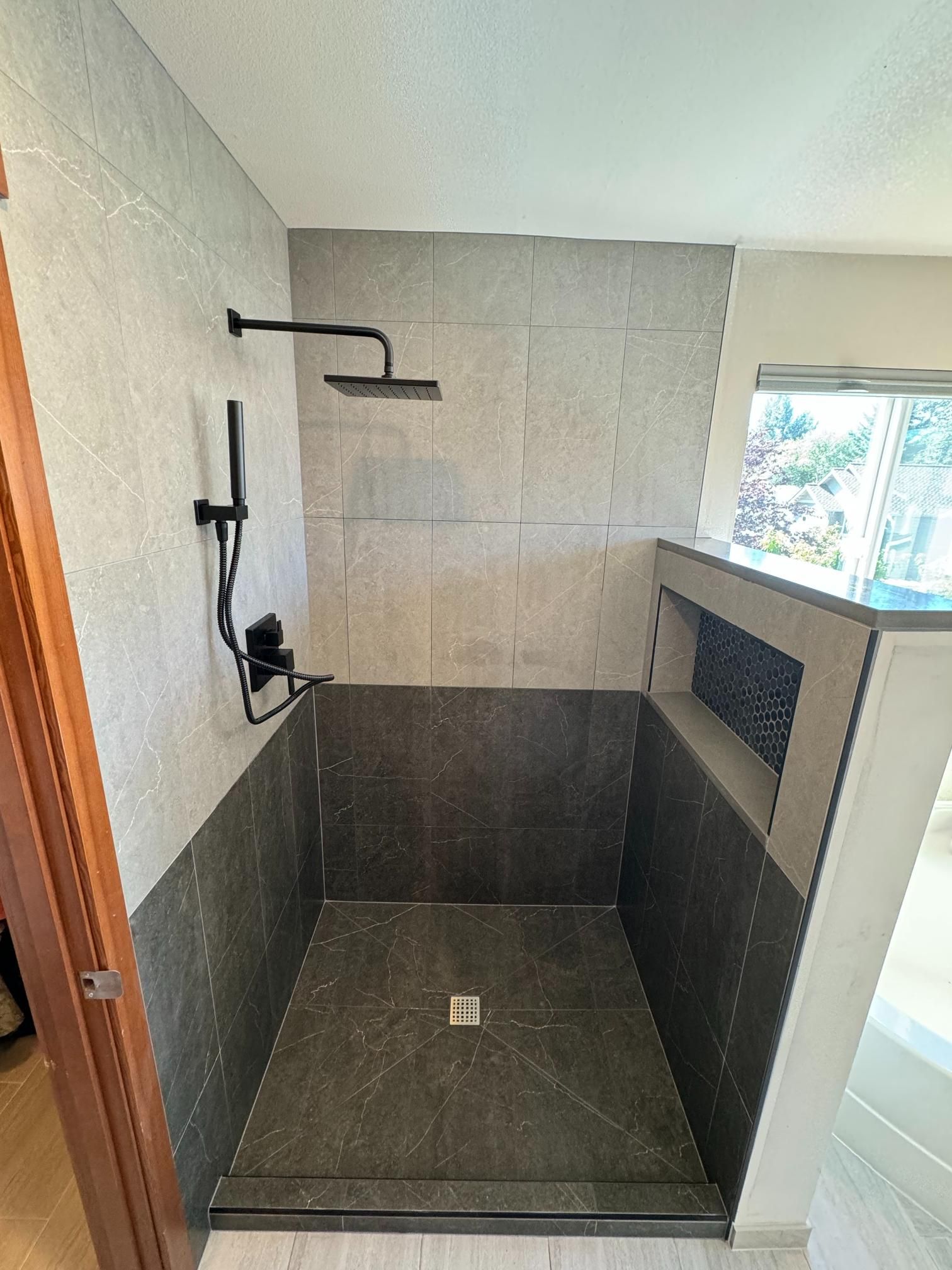 Walk-in shower with dark gray and light gray tiles, black shower fixtures.