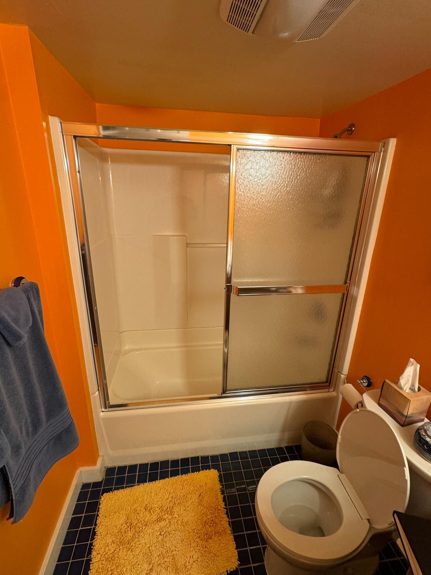 Bathroom with orange walls, a shower/tub, and a toilet. Blue towel and yellow rug visible.