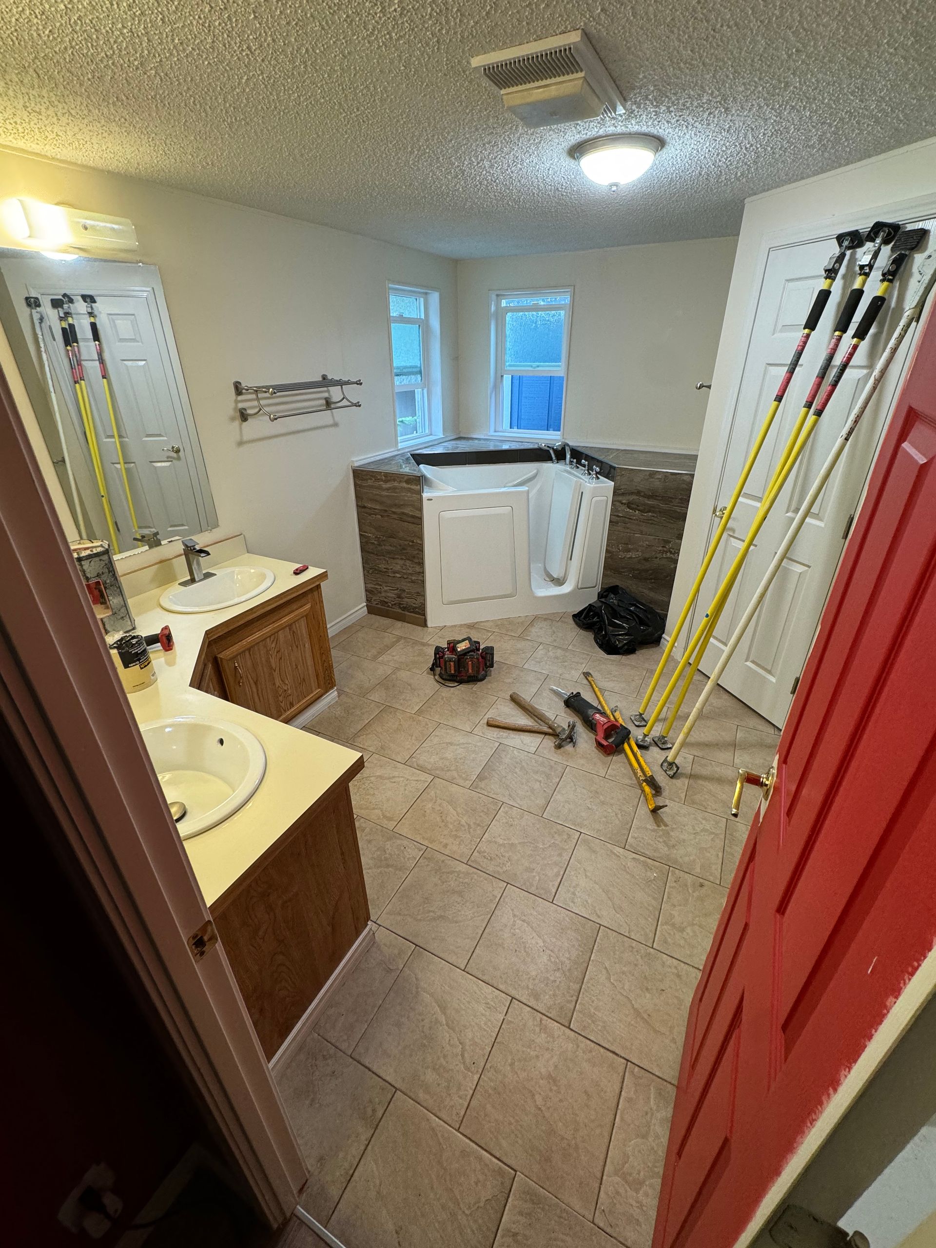 Bathroom renovation with walk-in tub and double vanity. Tools and equipment scattered on floor.