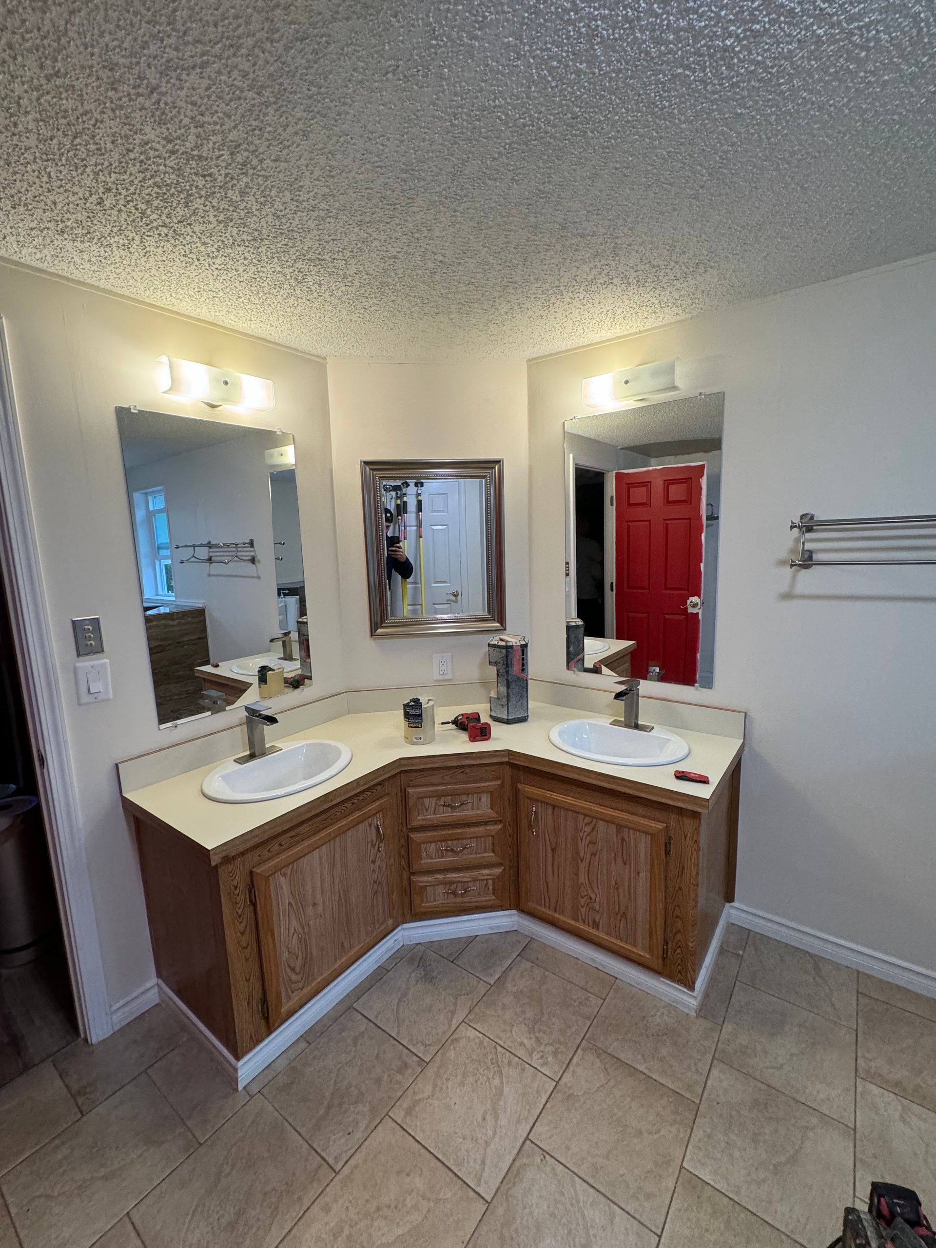 Bathroom with two sinks, mirrors, and wooden cabinets. Beige countertops, tan tile floor, and white walls.
