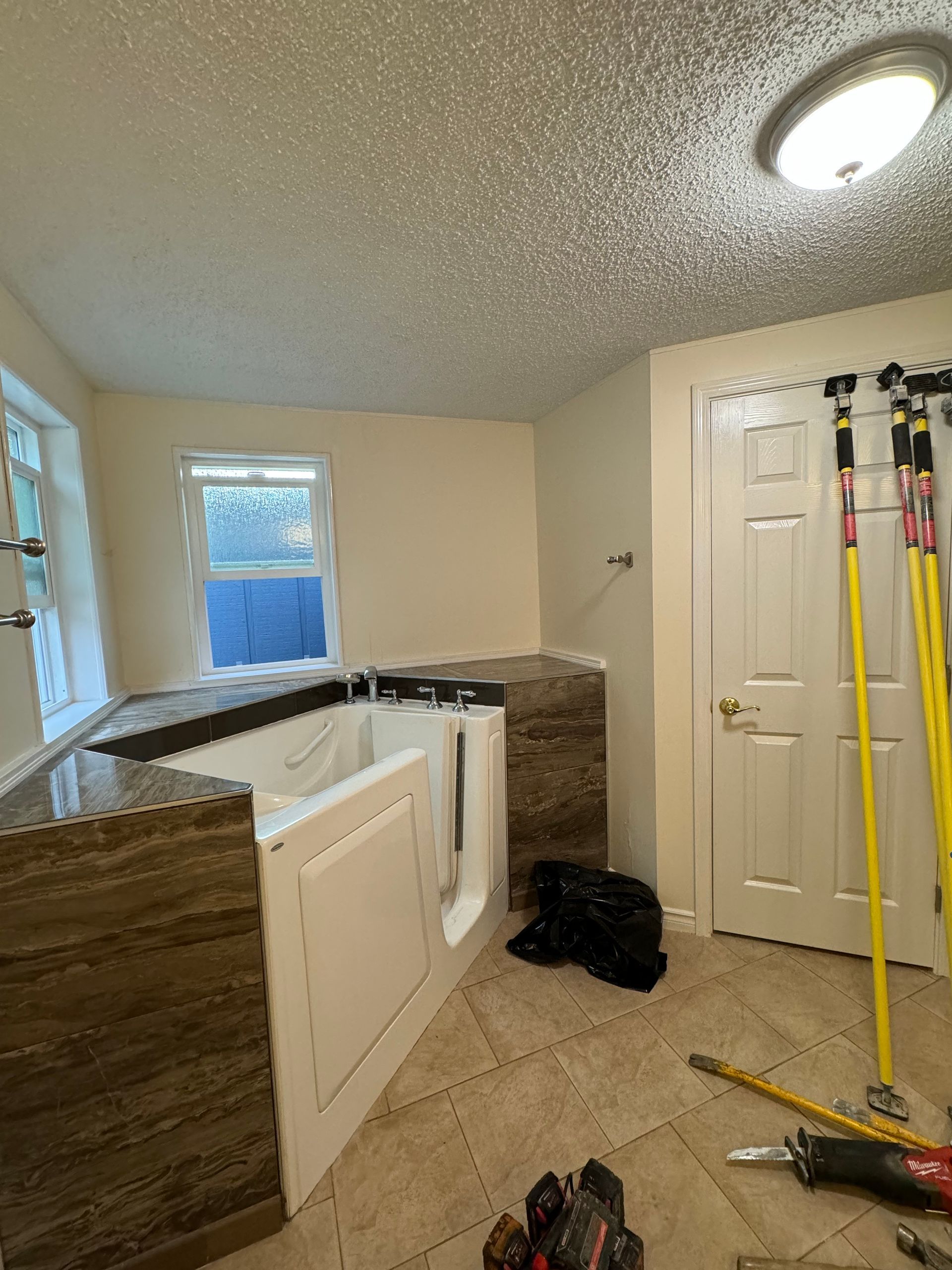 Bathroom with a walk-in tub, tiled floor, and a closed white door. Construction tools are present.
