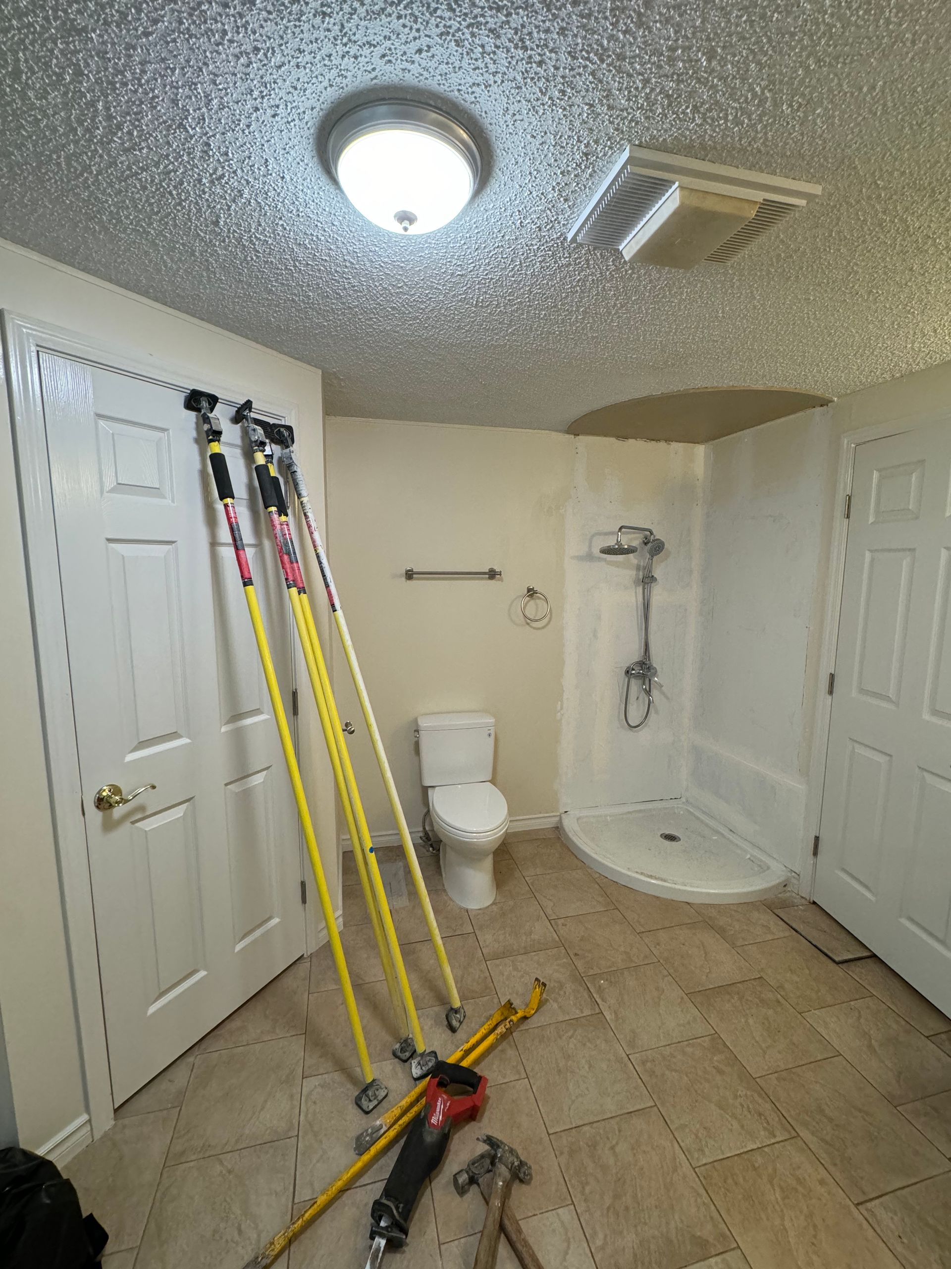 Bathroom renovation in progress; tools, toilet, shower, and ceiling light.