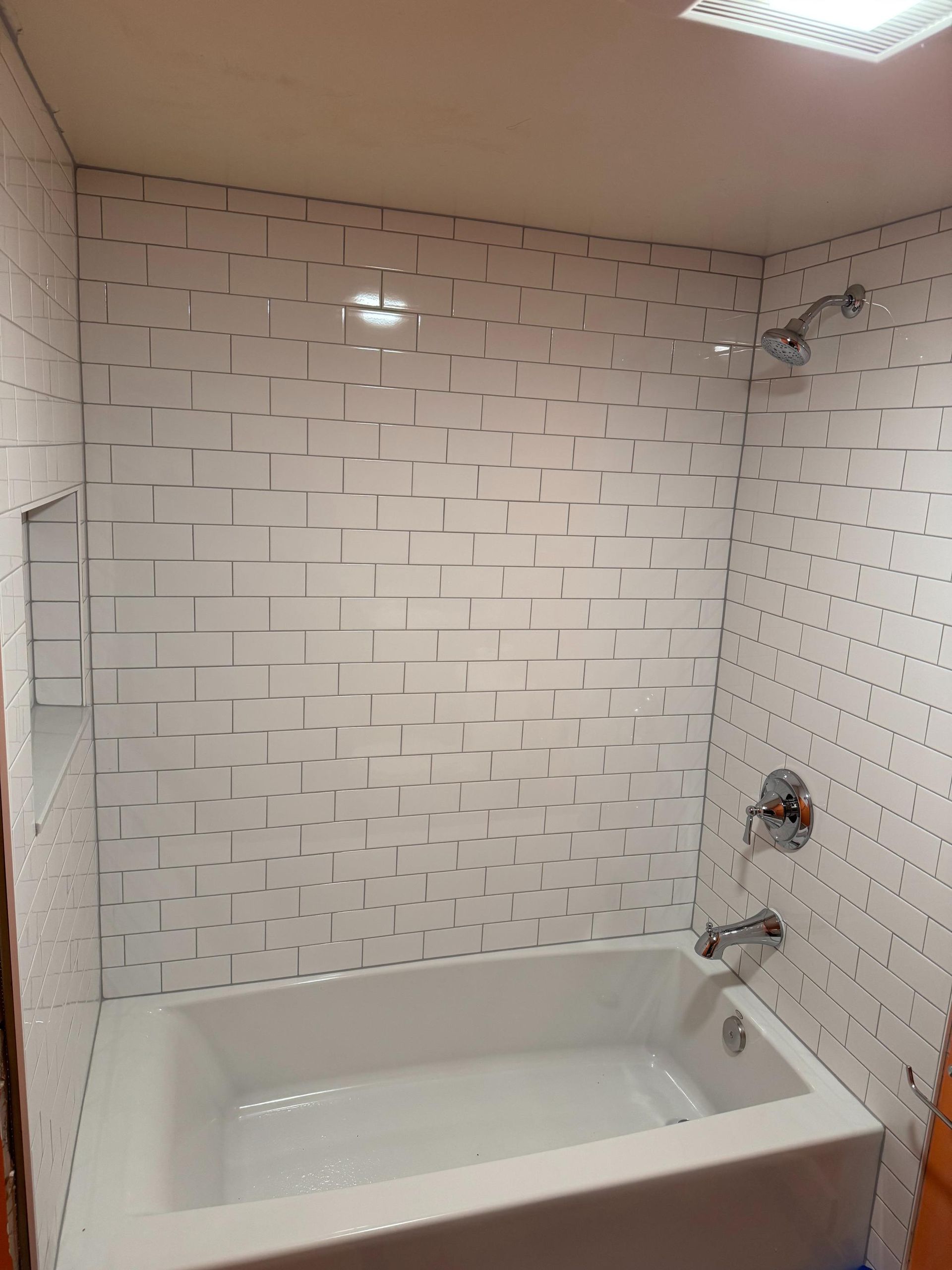 White-tiled shower with a built-in shelf, bathtub, and chrome fixtures.