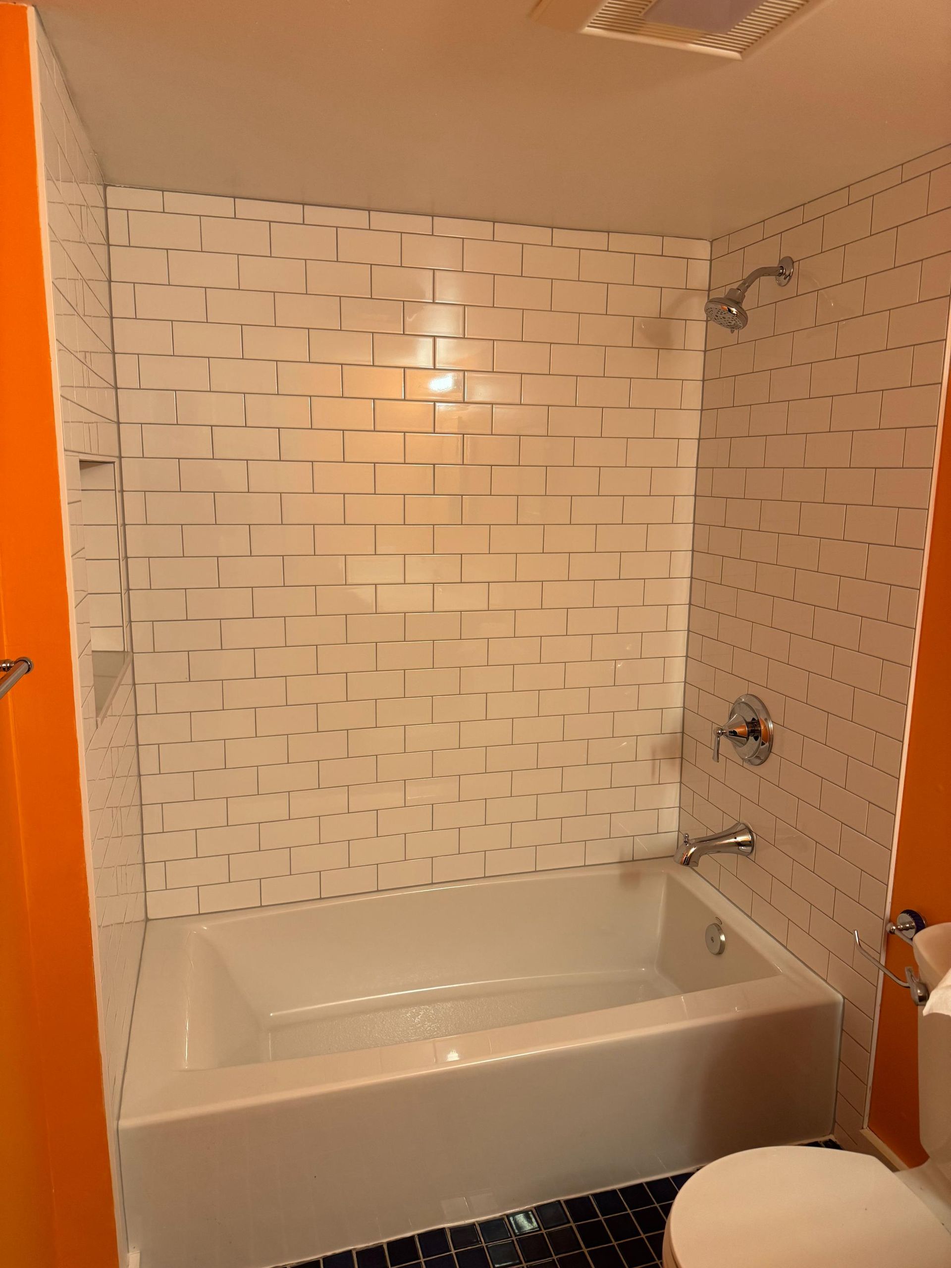 White tiled shower with tub and chrome fixtures in a bathroom with orange walls.