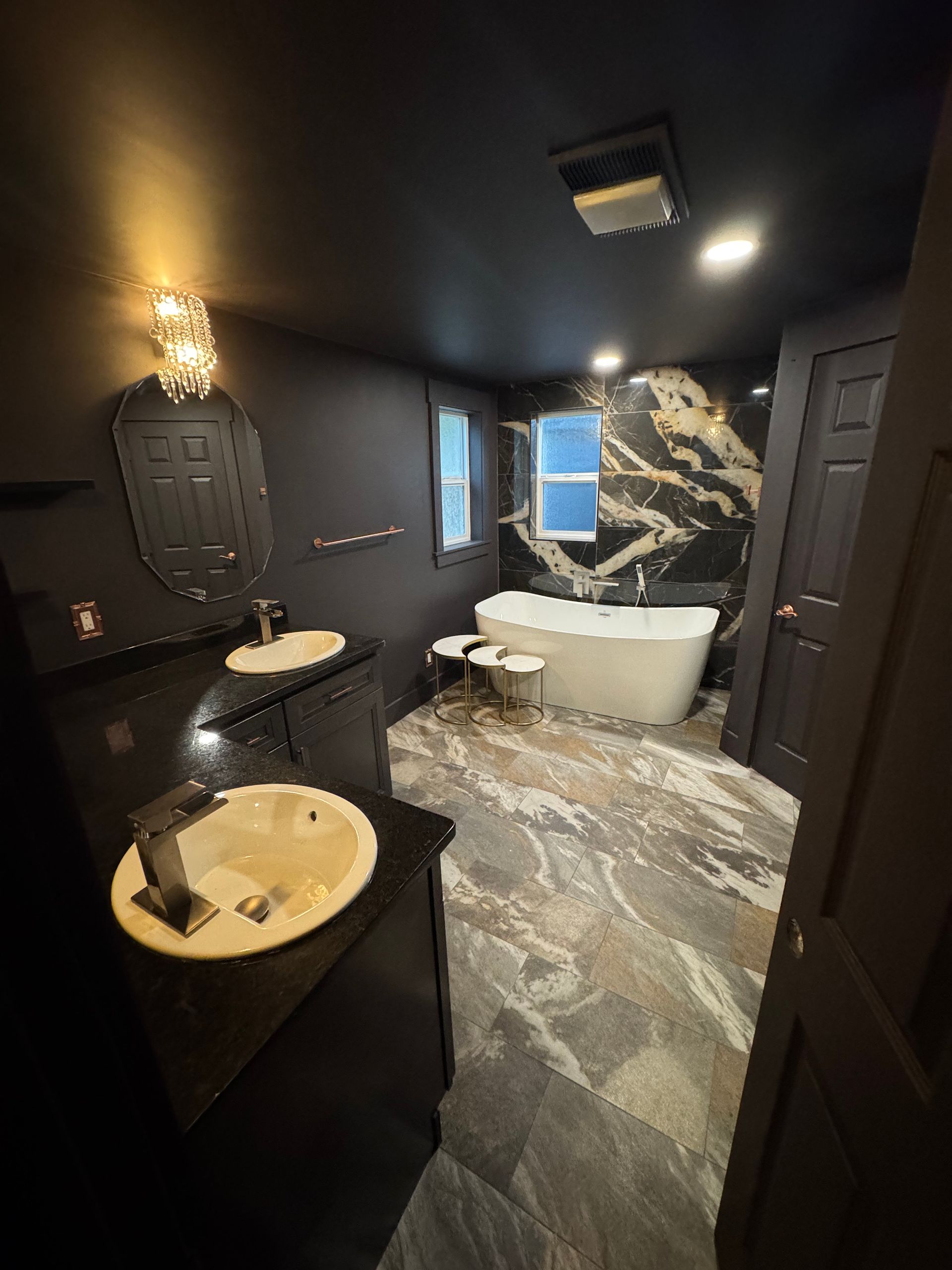 Dark bathroom with black walls, marble tile, a soaking tub, and double sinks.