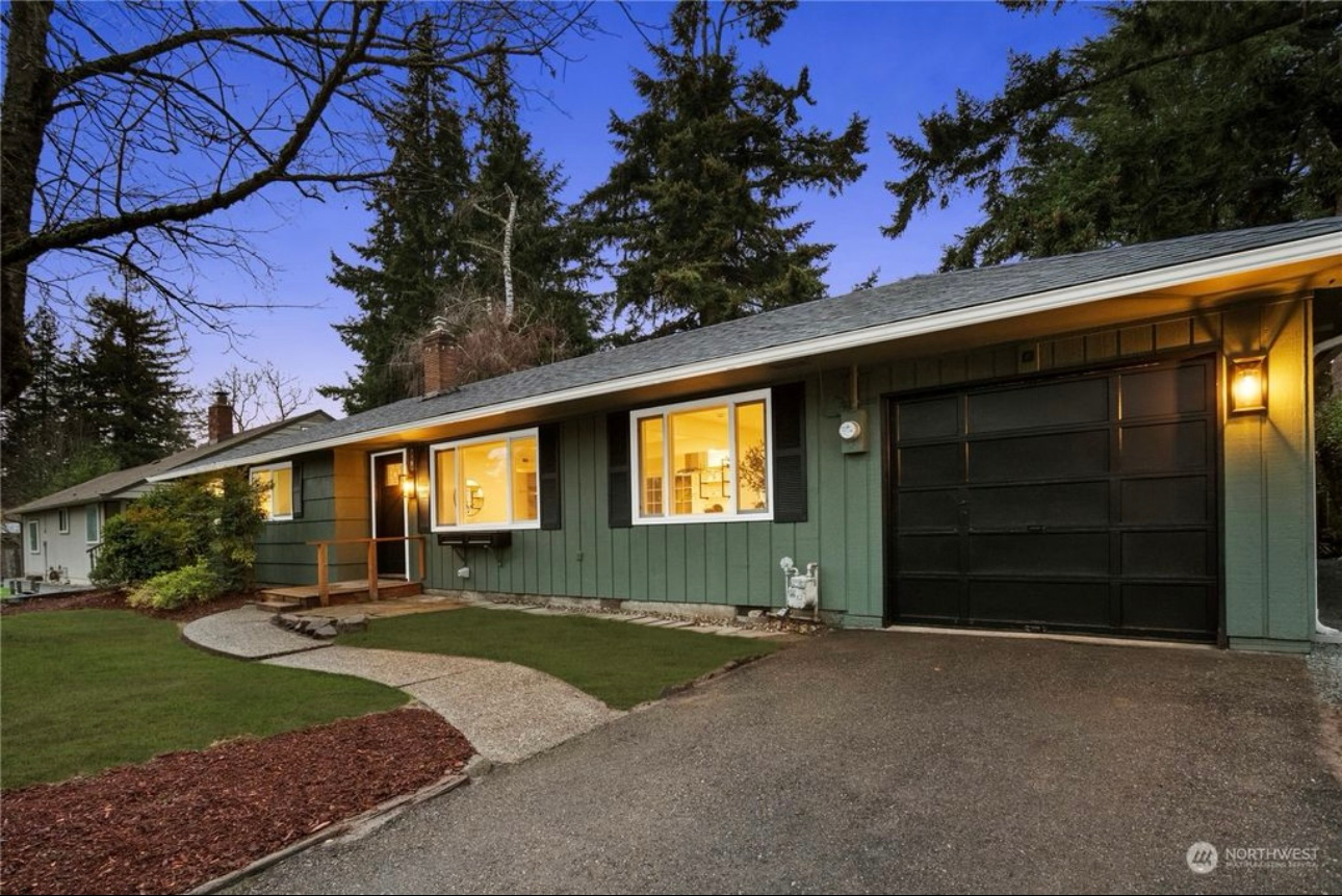 Green house with a black garage door and walkway leading to the front door at dusk.