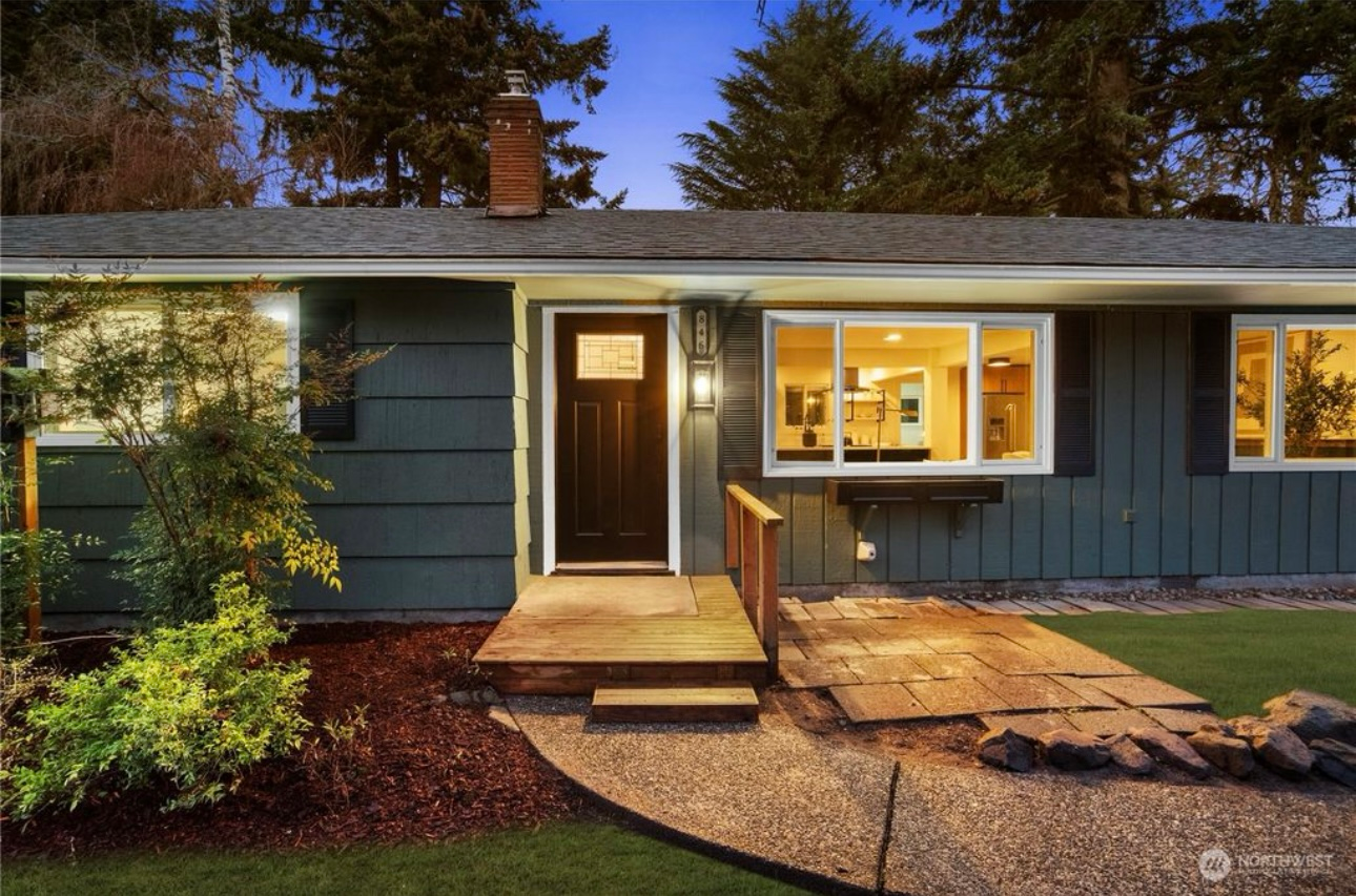 Exterior of a teal-colored house with a dark brown door, windows, and a small walkway at dusk.