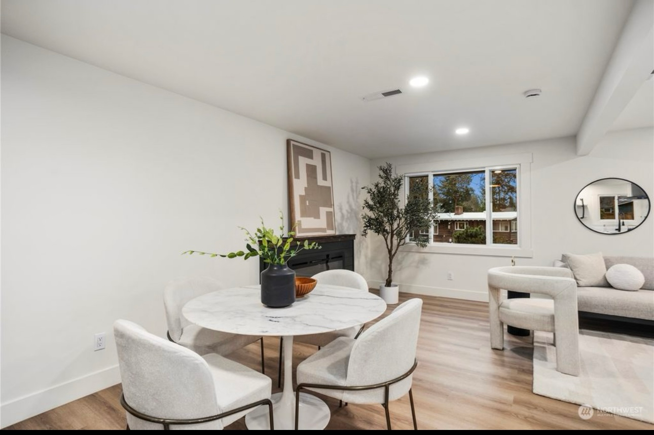 Dining area with white table, chairs, and fireplace; living area with couch, large window.