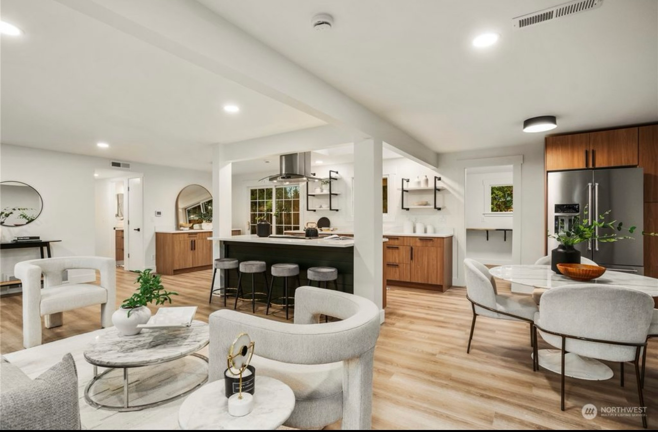 Open-concept kitchen and living area, featuring light wood floors, white walls, and modern furniture.