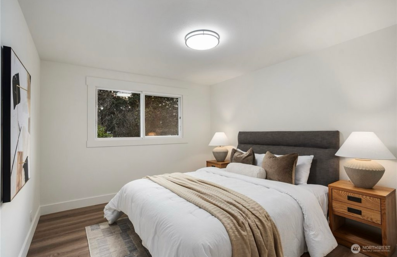 Bedroom with bed, nightstands, window, and artwork. White walls, wood floor, neutral tones.