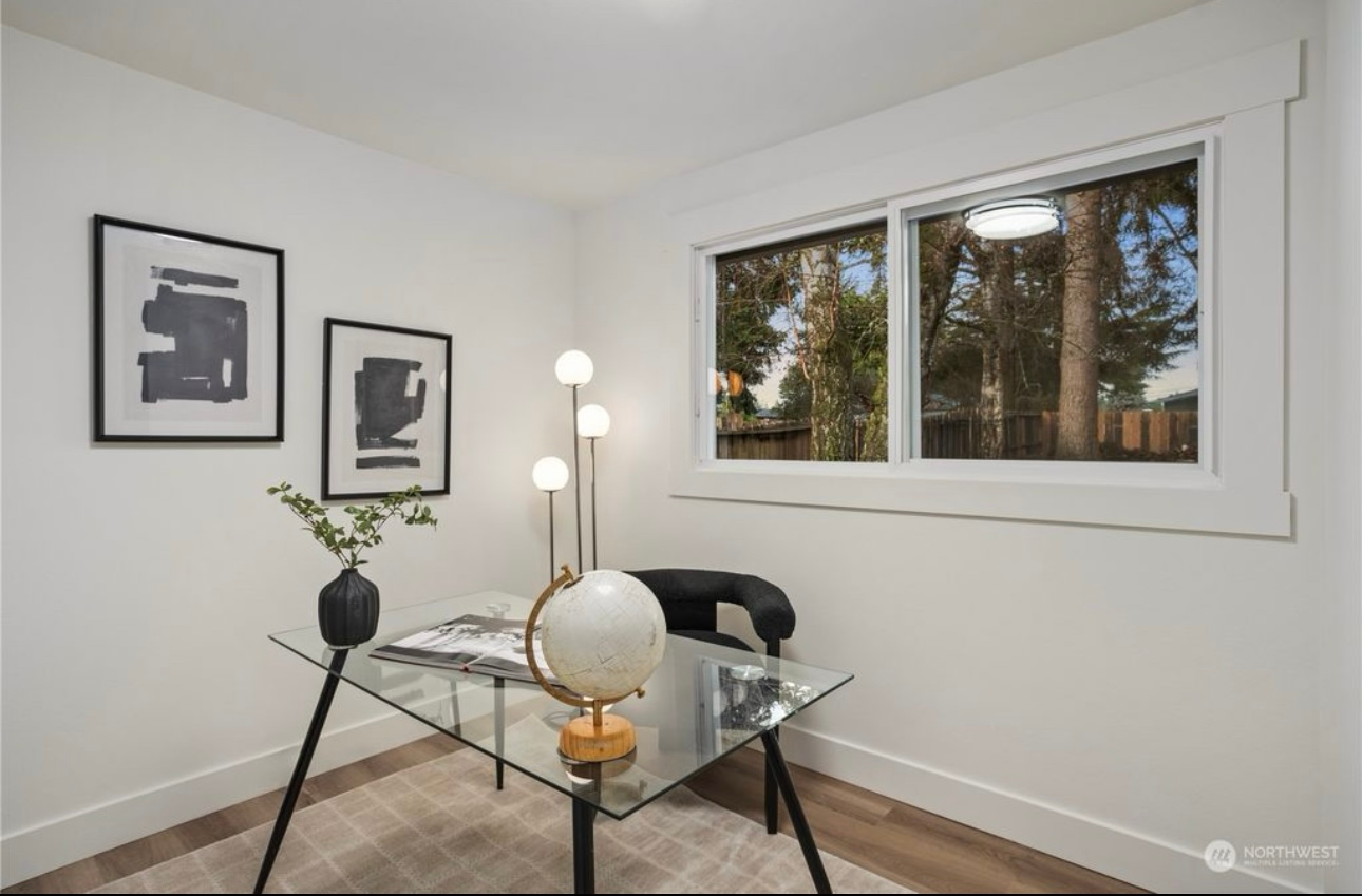 Home office with glass desk, lamp, two framed artworks, and a window.