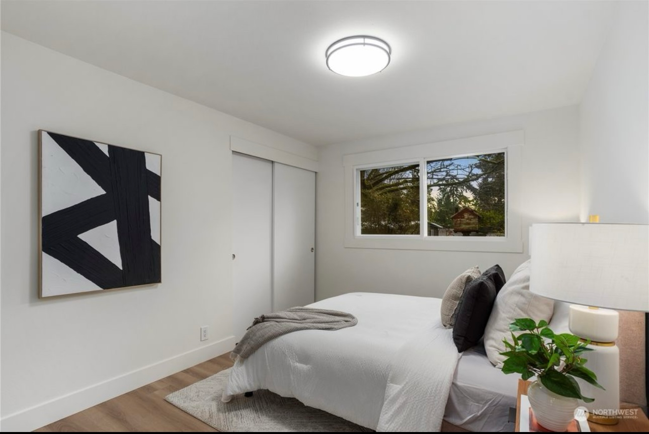 Bedroom with white walls, bed, abstract art, and a window overlooking greenery.