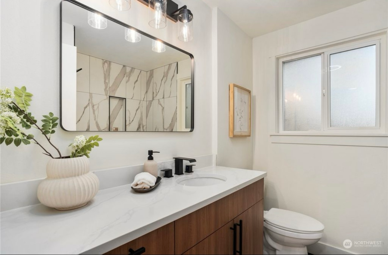 Modern bathroom with wood vanity, white countertop, and marble accent wall.