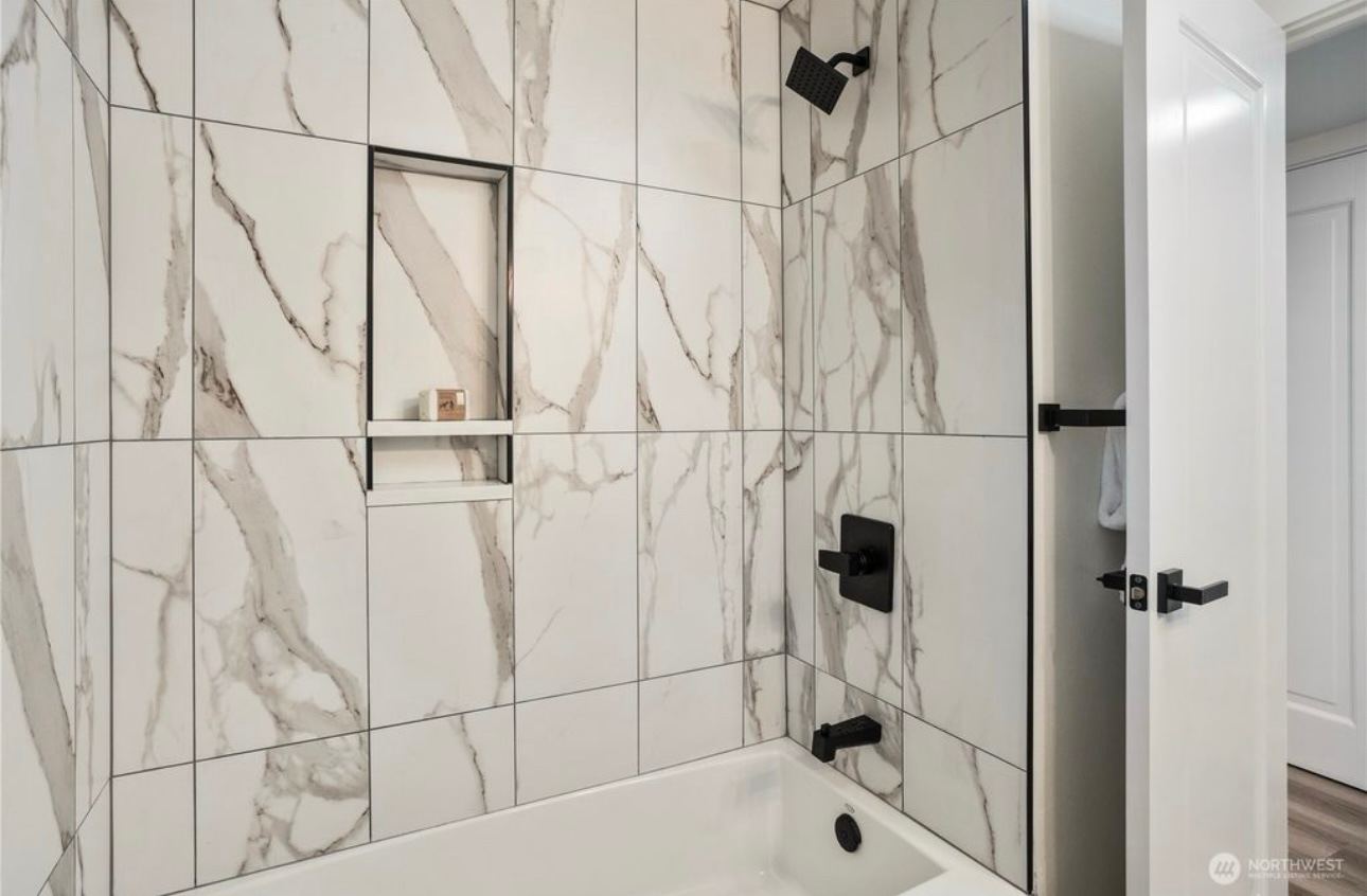 Modern bathroom with marble-patterned tile, black fixtures, recessed shelf, and white door.