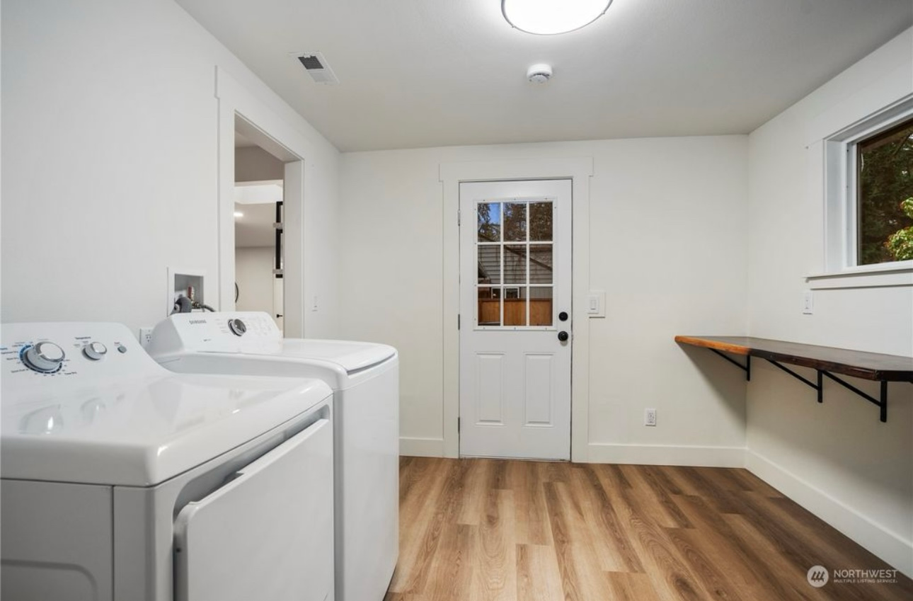 Laundry room with white appliances, door, and a wooden shelf.