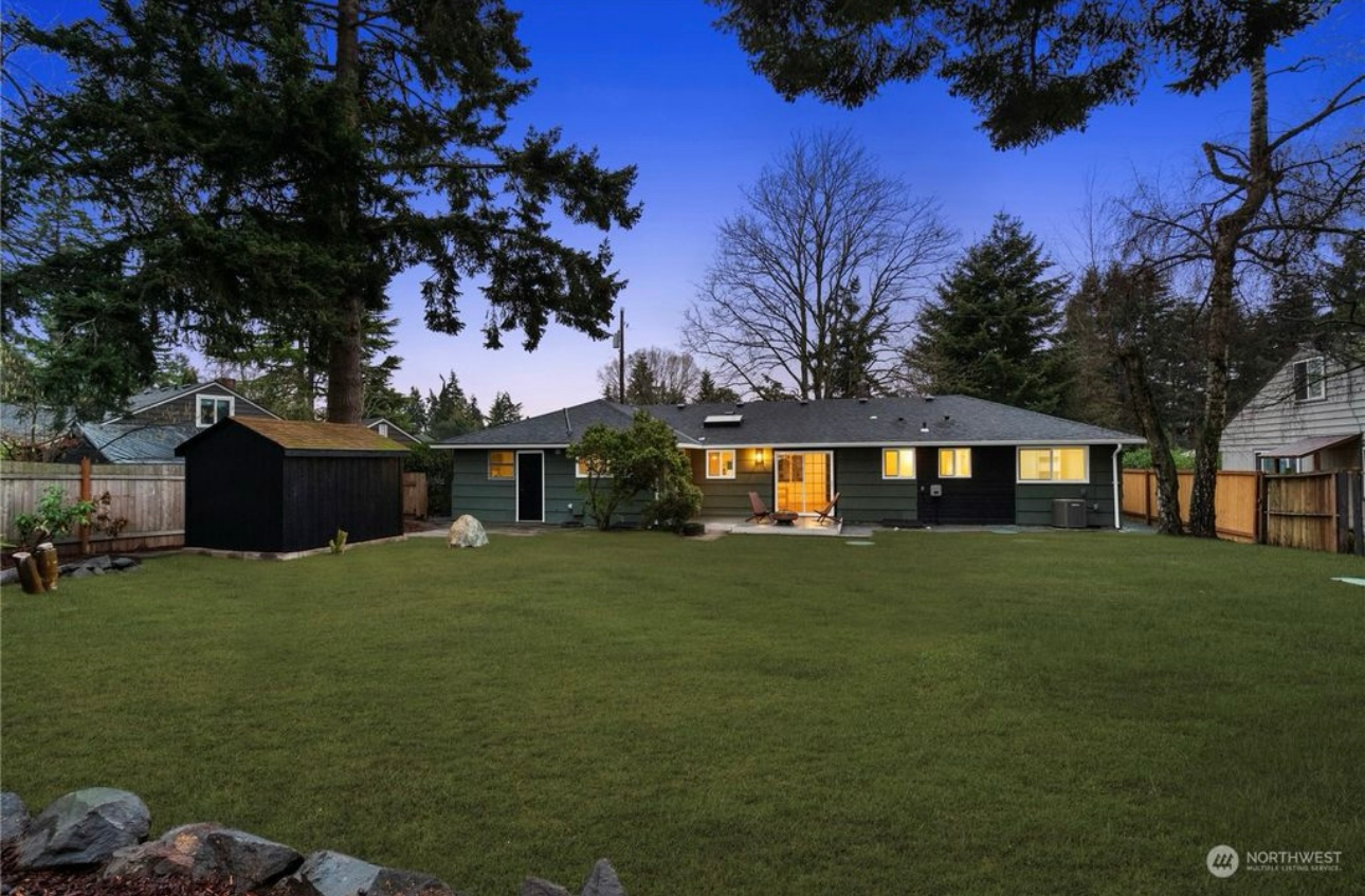 Backyard view of a single-story house with green exterior and a large lawn at dusk.