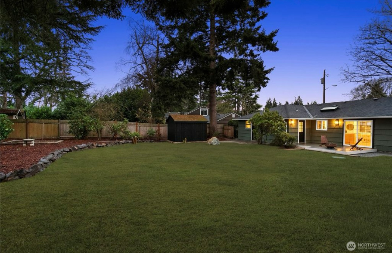 Backyard with green lawn, shed, and low-slung house under a twilight sky.