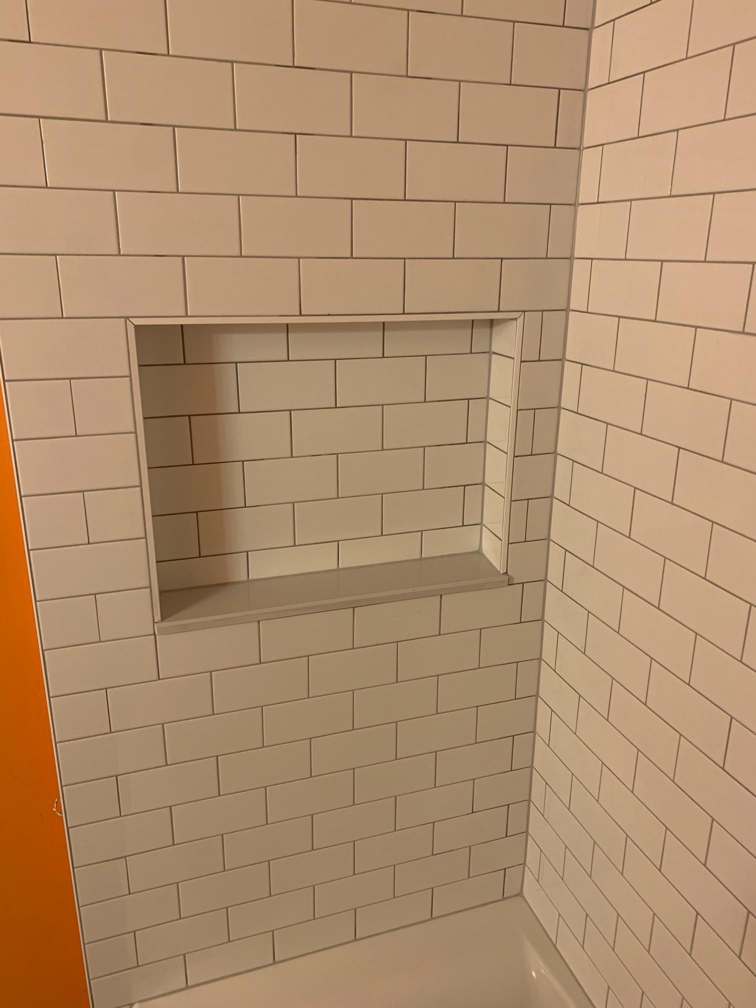 White tiled shower with a built-in shelf.