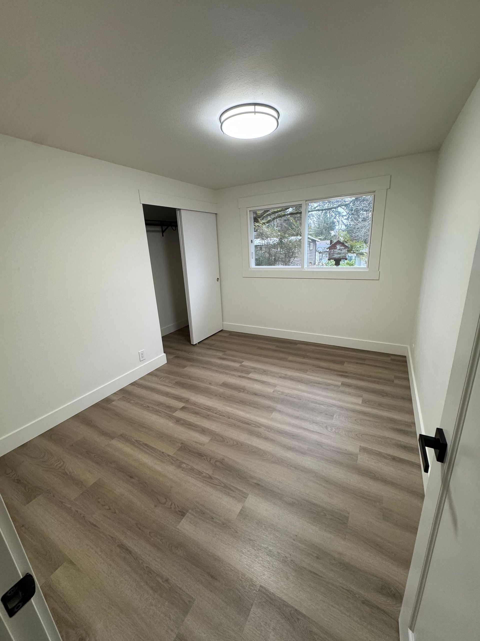 Empty room with light wood-look floor, white walls, closet, window, and ceiling light.