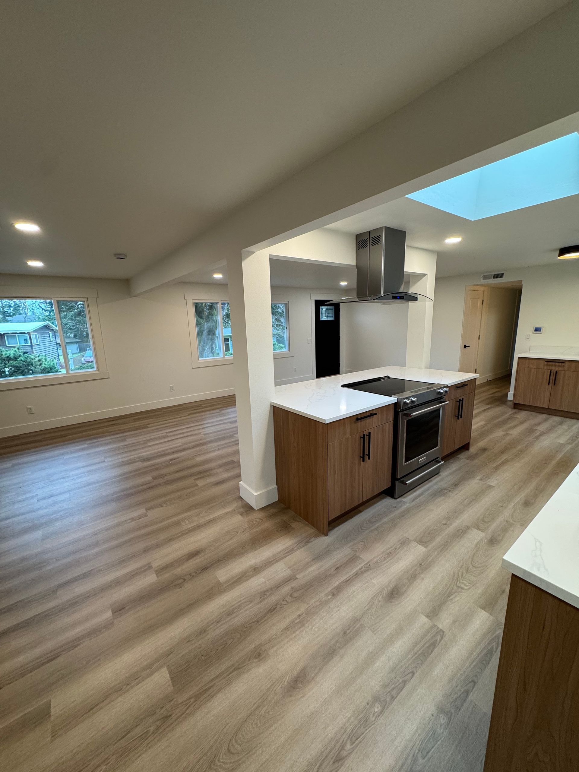 Modern kitchen with wood cabinets, white countertops, and stainless steel range. Wooden floors and recessed lighting.