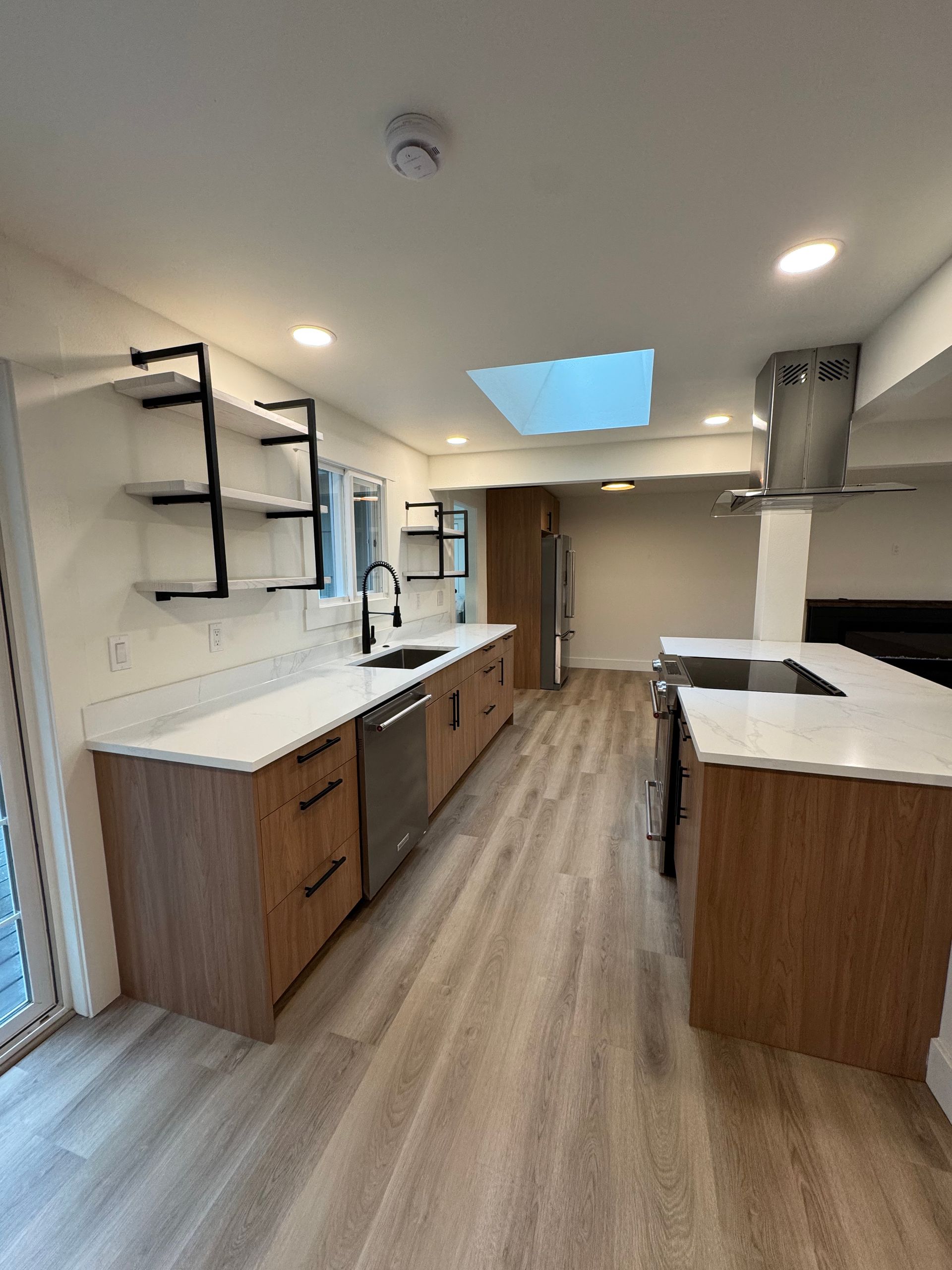 Modern kitchen with wood cabinets, white countertops, black faucet, stainless steel appliances, and skylight.