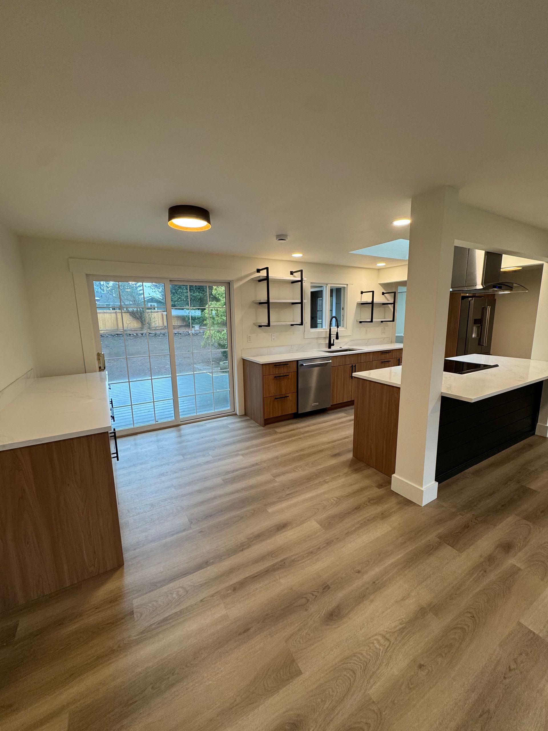 Modern kitchen with wood cabinets, white countertops, and stainless steel appliances. Sliding glass door leads to patio.
