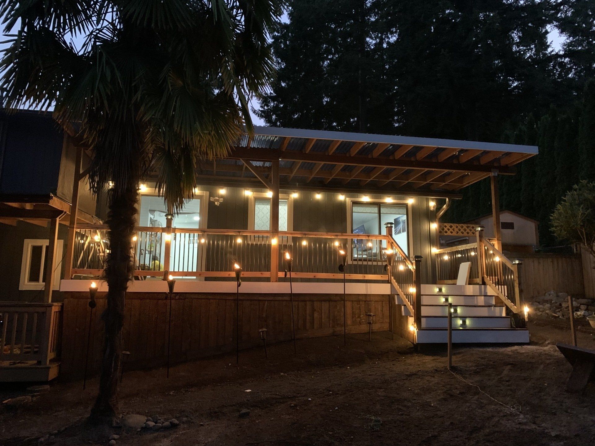 A house at night with string lights and tiki torches illuminating the deck and palm tree.