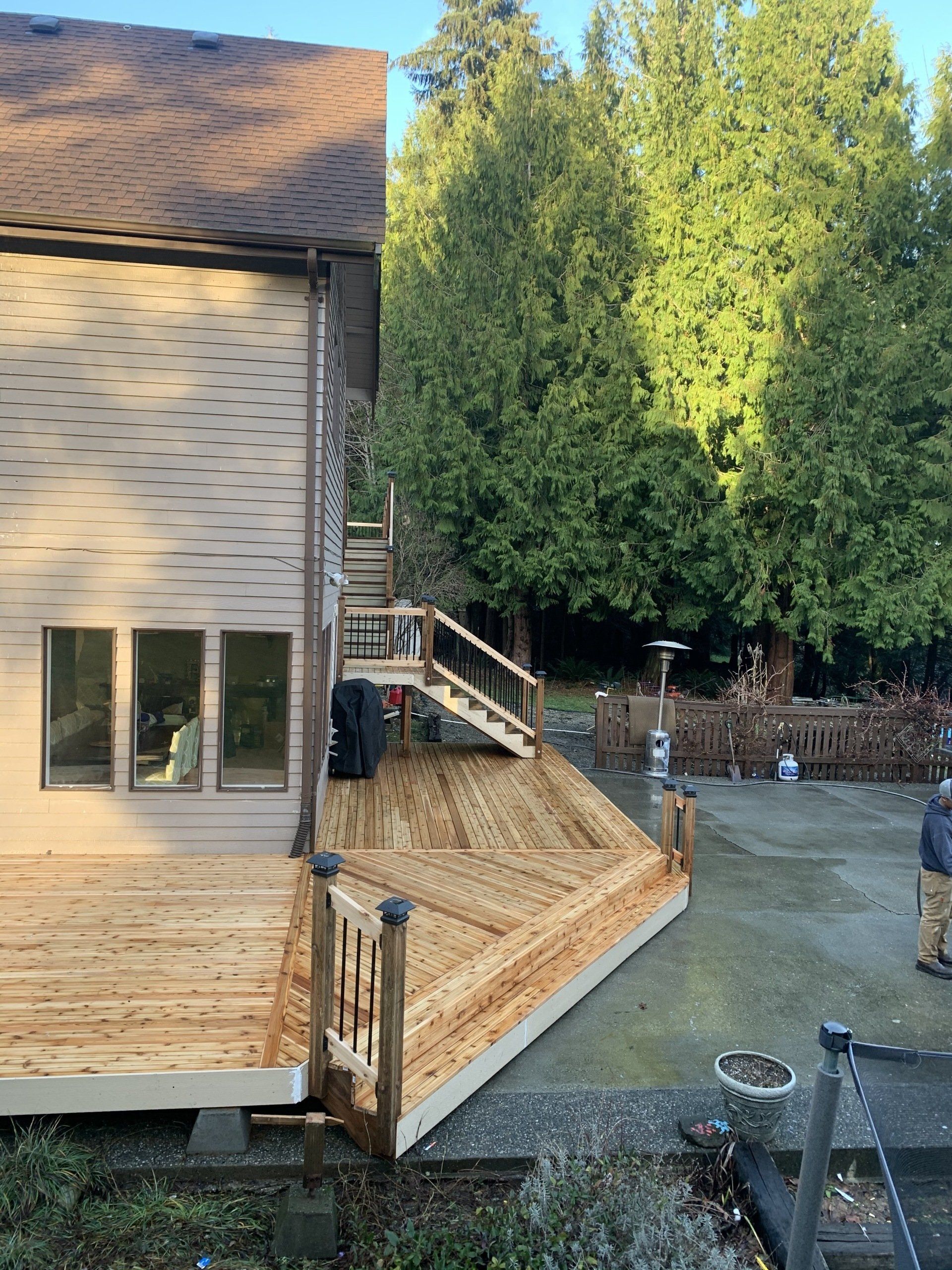 Wooden deck with stairs, built against a house with a brown roof and siding. Deck leads to a yard.