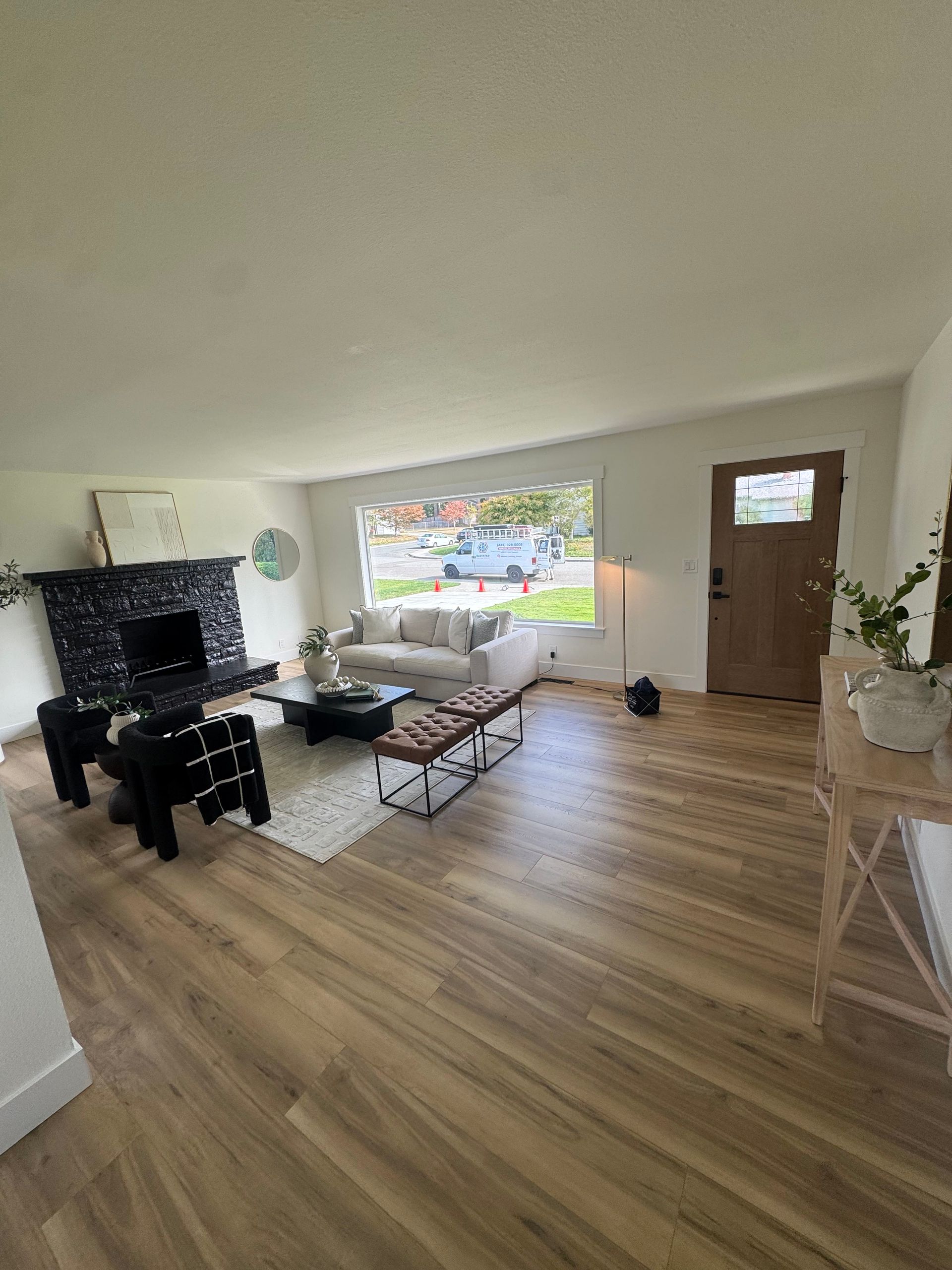 Modern living room with a black fireplace, white accent wall, built-in bench, and wood shelves.