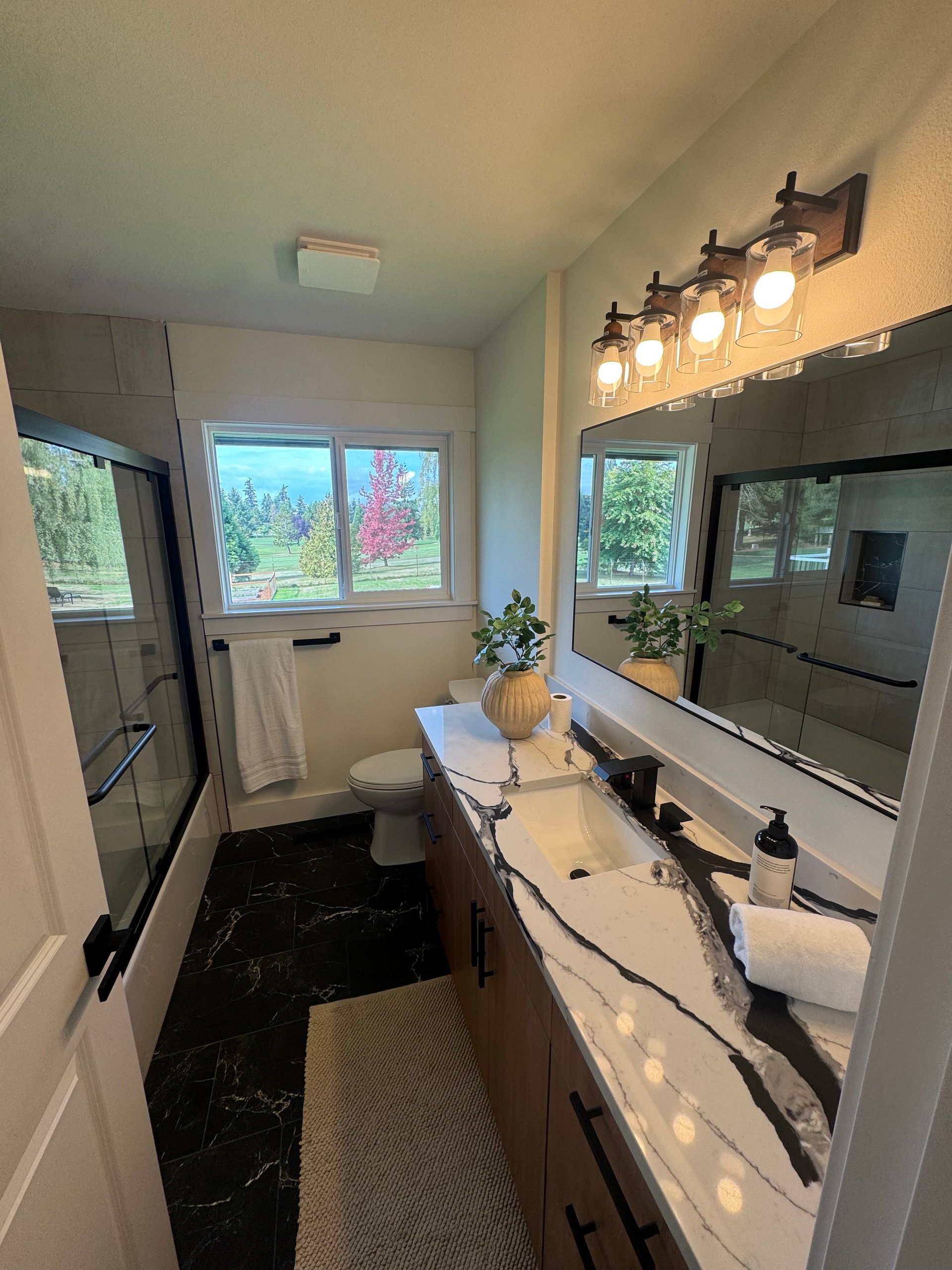 Dark bathroom with dual sinks, mirrors, and crystal chandeliers. Black cabinets, countertops, and walls.