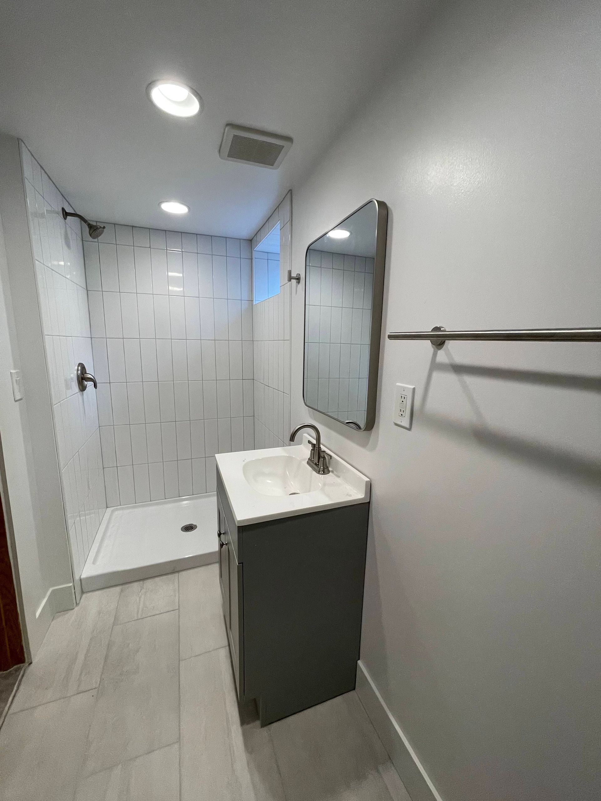 Bathroom with a gray vanity, shower with white tiled walls, and a silver towel rack.