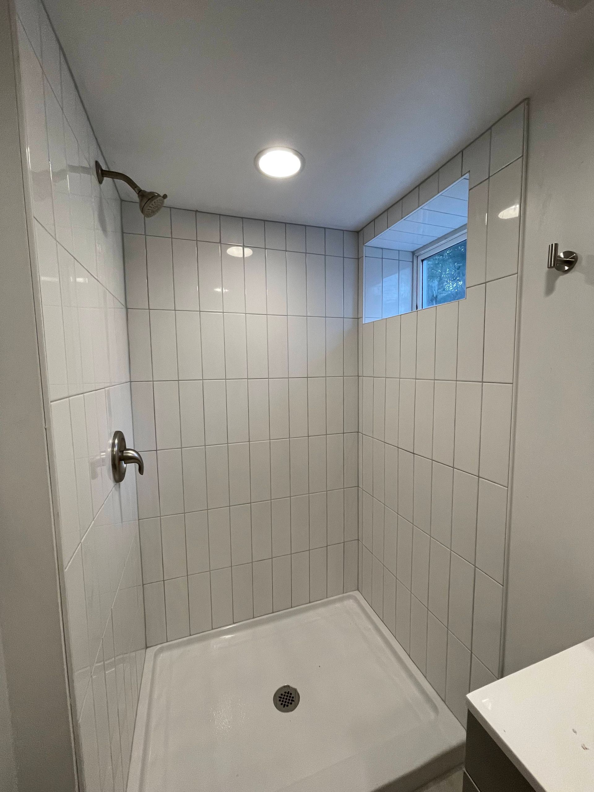 White tiled shower with a gray base and a small window.