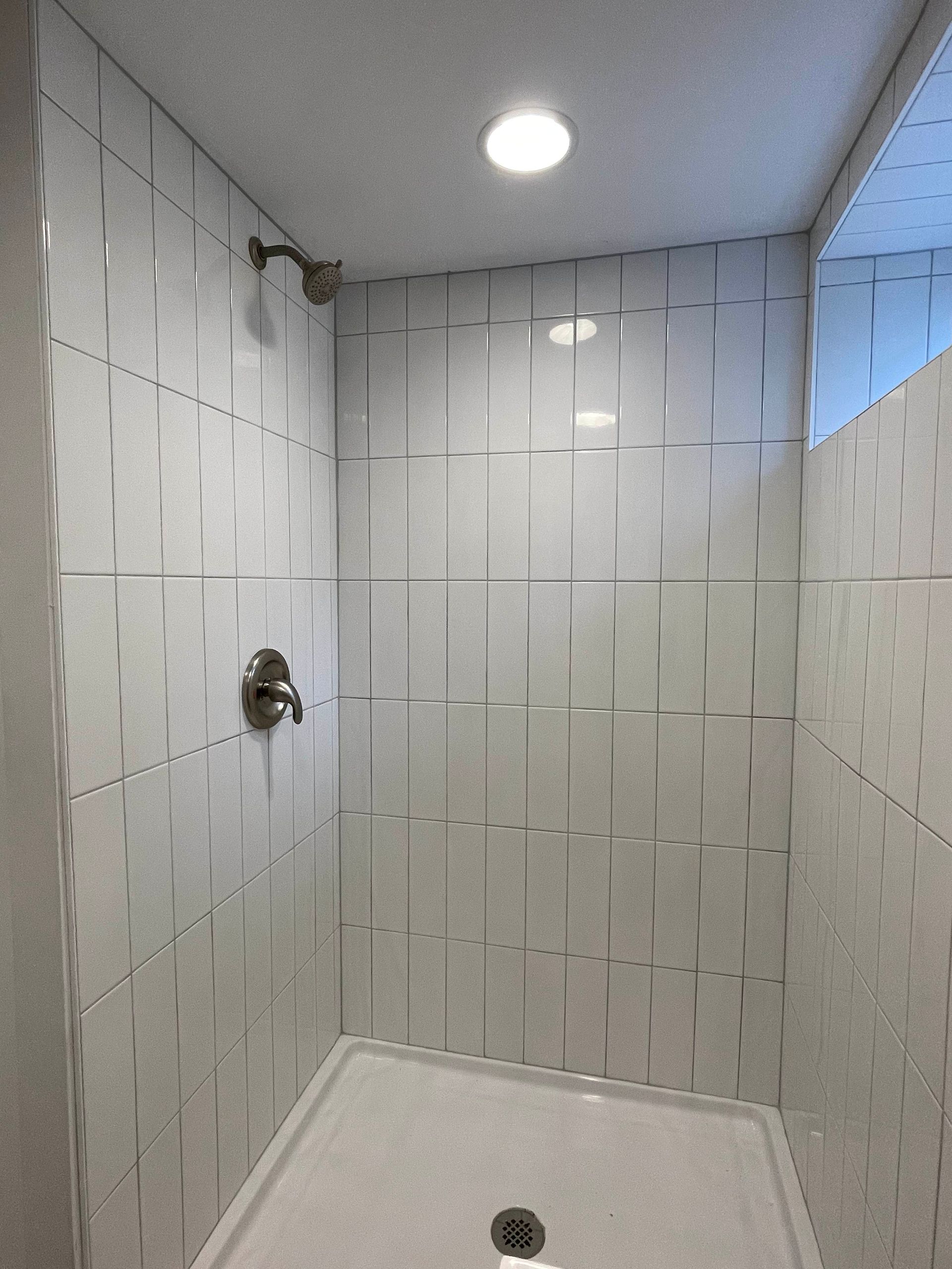 White tiled shower with glass panel, silver fixtures, and recessed lighting.