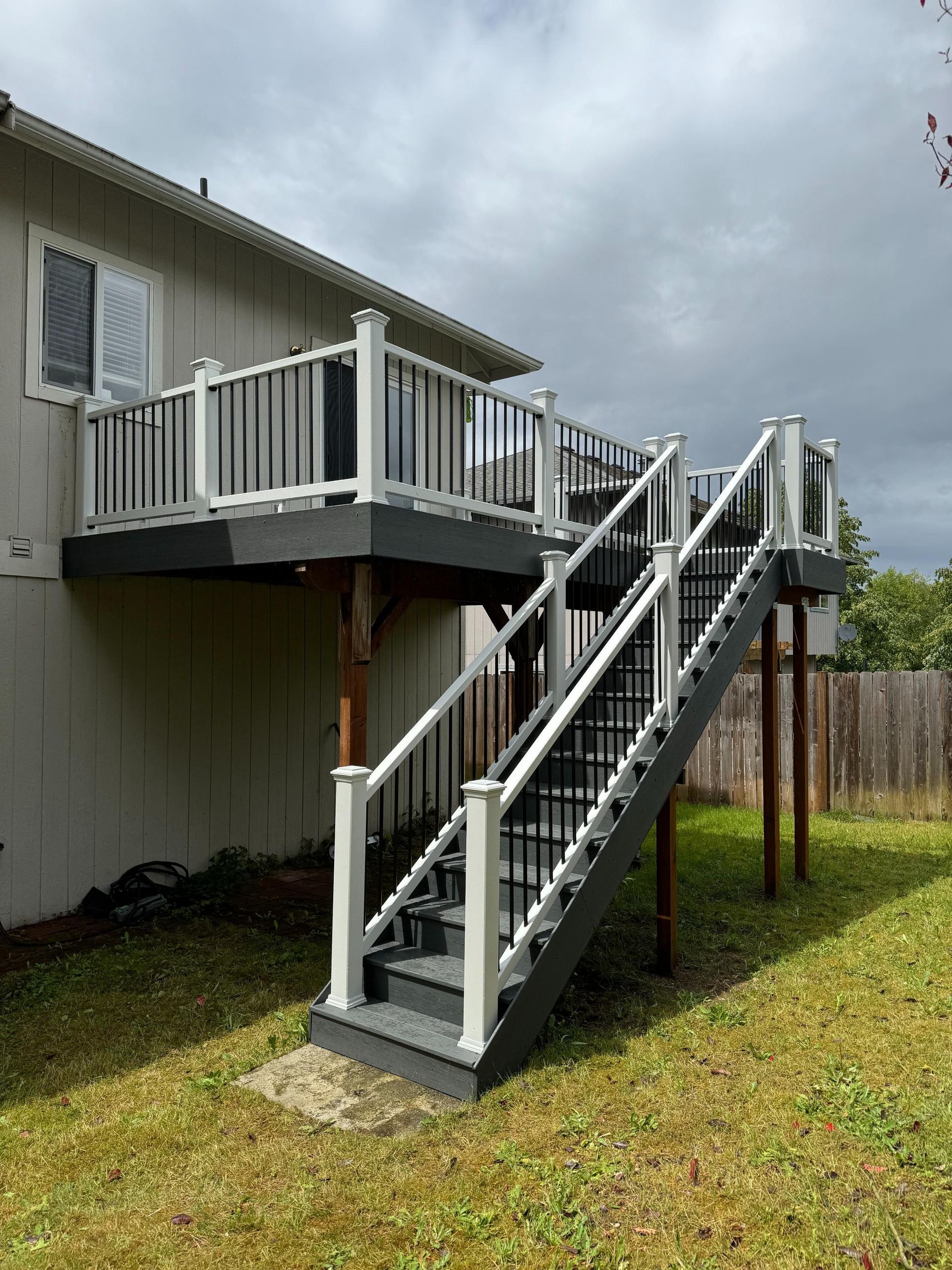 Gray and white deck with stairs attached to a house, set in a grassy yard.