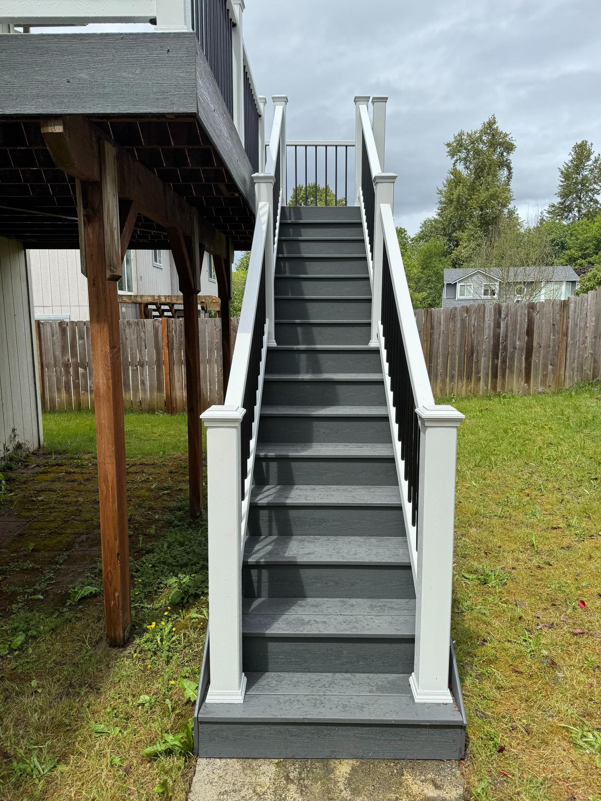 Outdoor staircase with gray steps and white railing leading up to a deck.