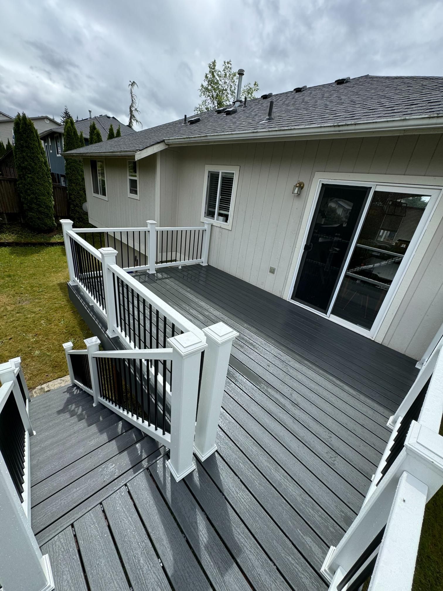 Gray deck with white railing, black spindles, leading to a house with sliding glass door.