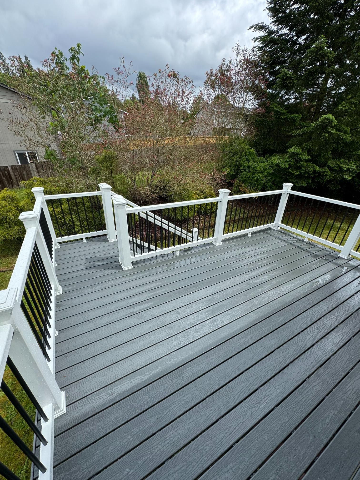 Gray deck with white railing and black spindles, overlooking a backyard with trees.