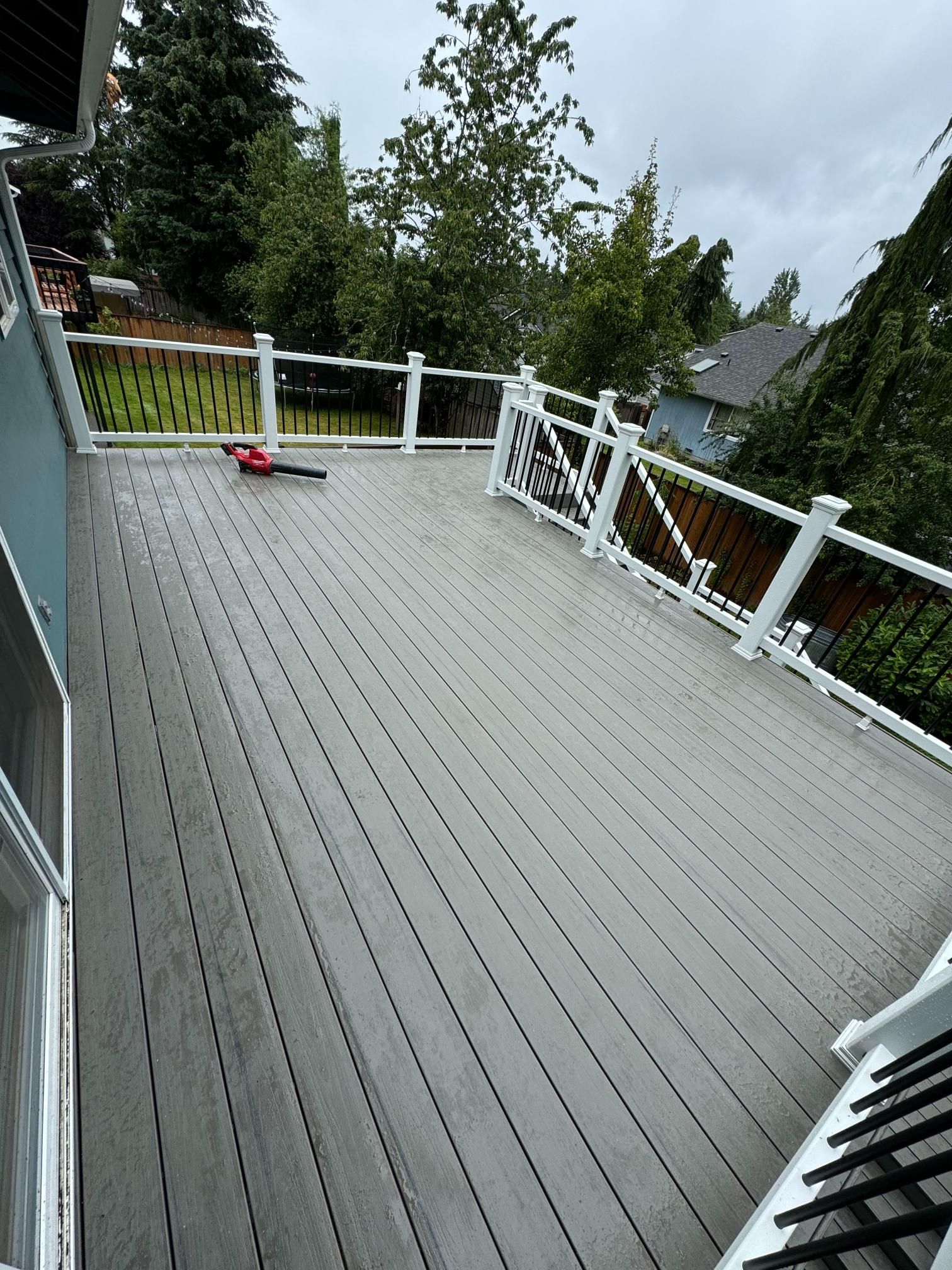 A gray composite deck with white railings overlooks a yard with trees under a cloudy sky.