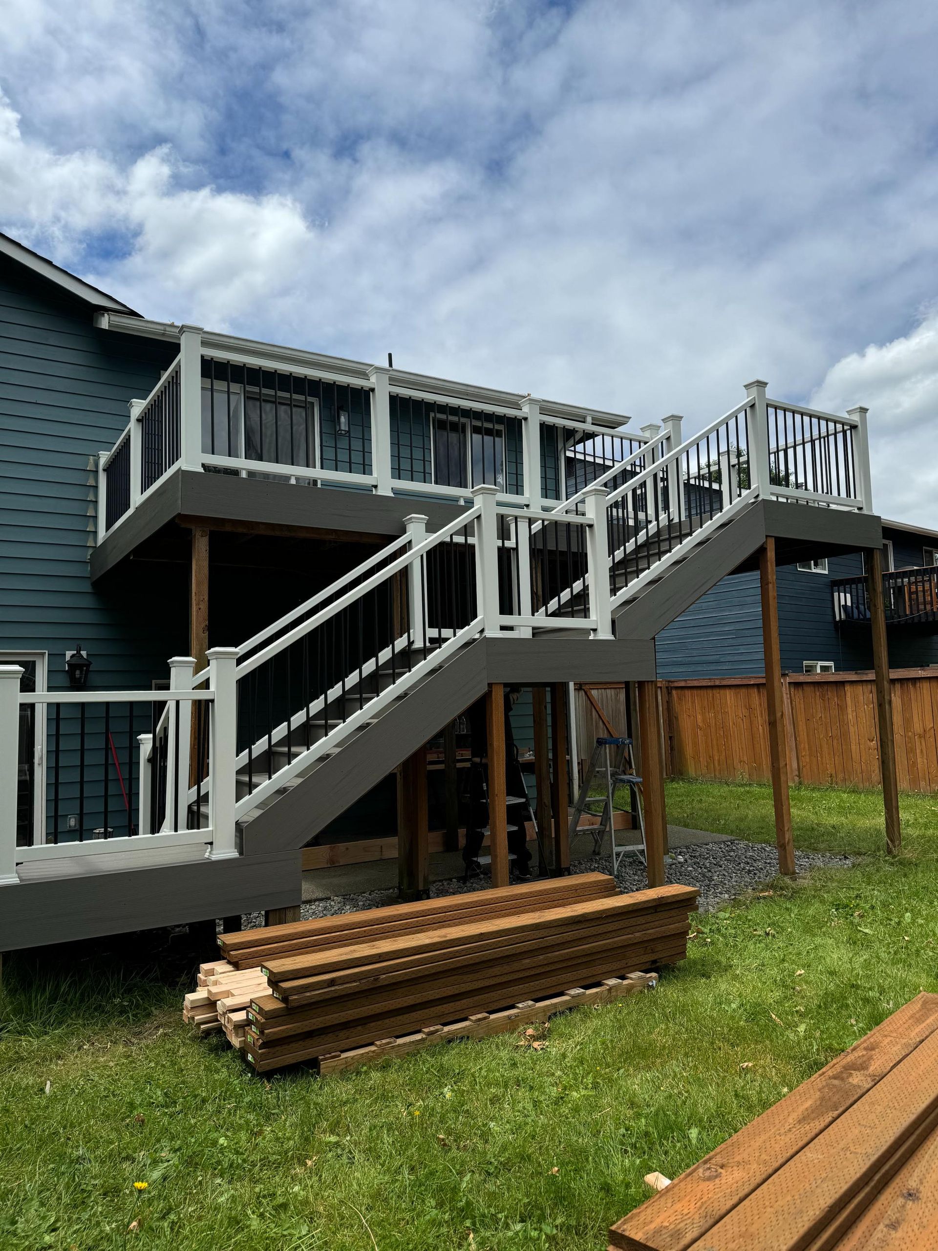 Two-level deck with gray and white railings attached to a blue house, stairs lead down to a grassy yard.