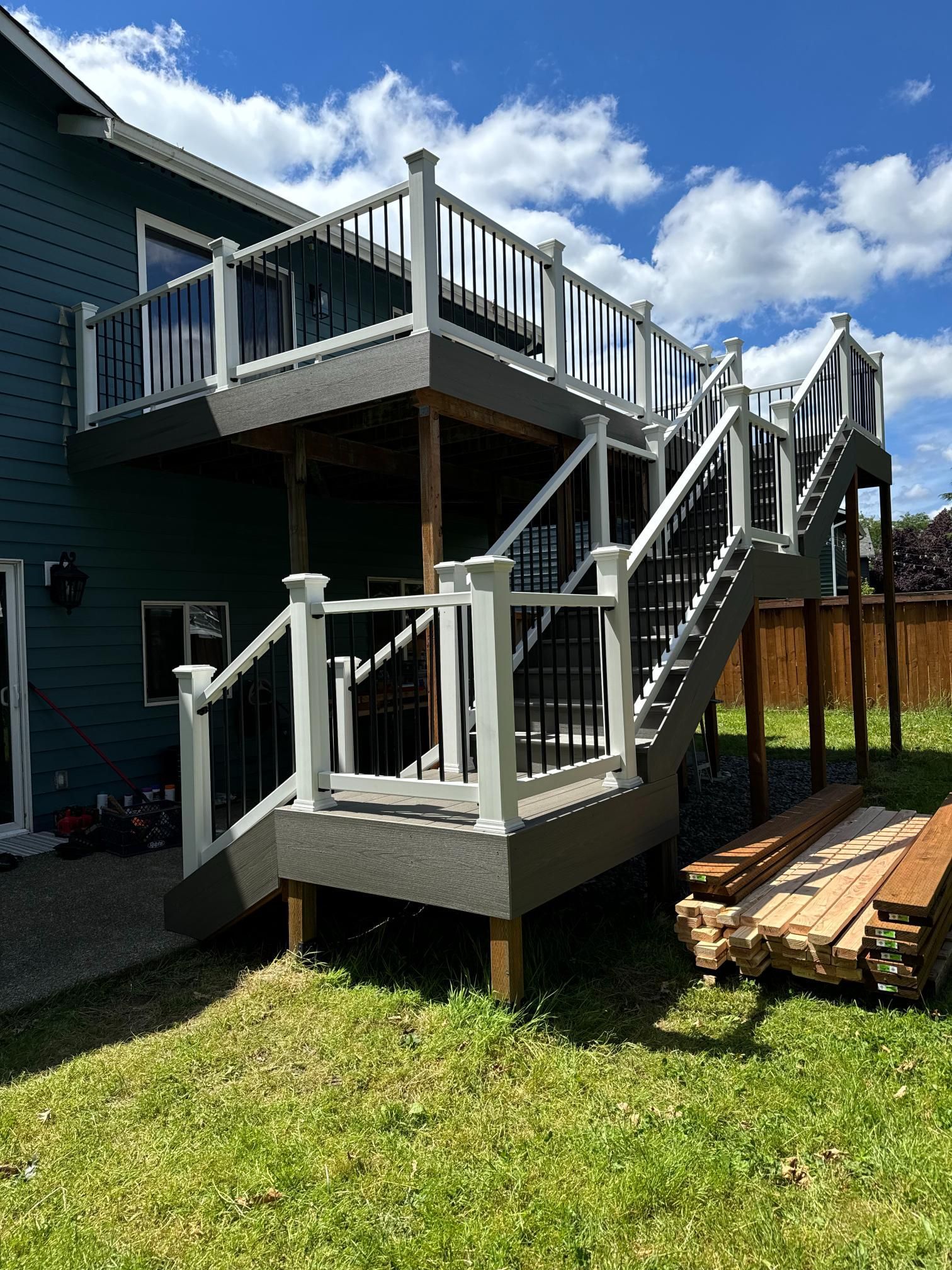 Two-level deck with white railings and black balusters attached to a dark blue house. Stairs lead down to a grassy yard.