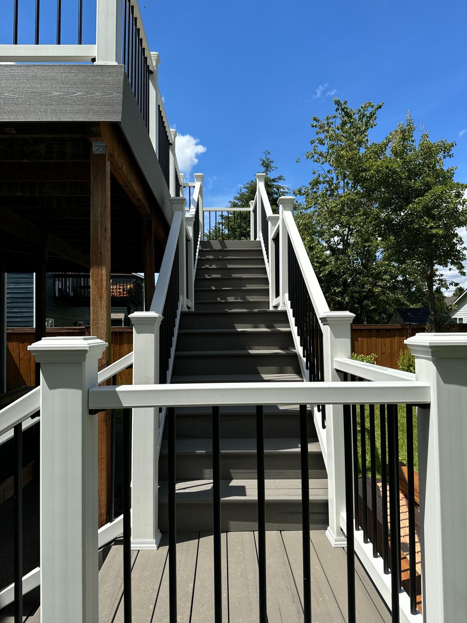 Gray staircase with white and black railings, leading to a wooden deck on a sunny day.