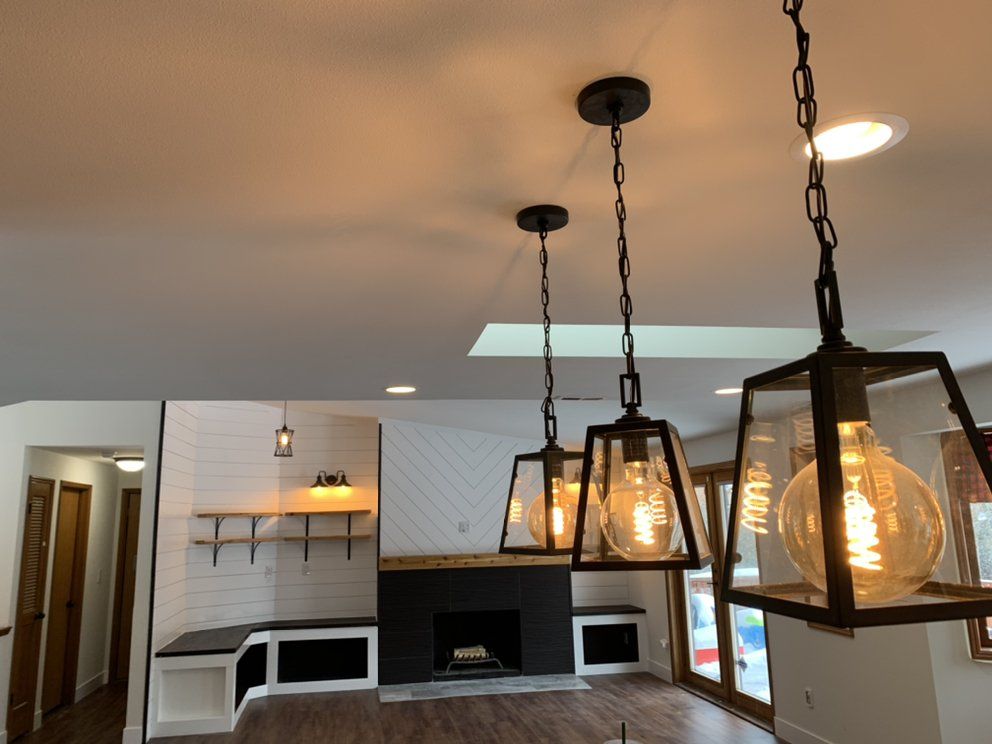 Three black pendant lights with large, glowing bulbs hang over a room with a fireplace.