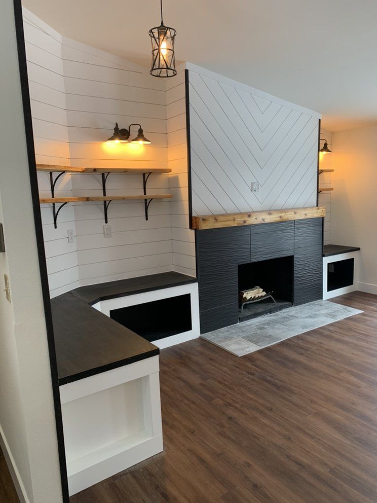 Modern living room with a black fireplace, white accent wall, built-in bench, and wood shelves.