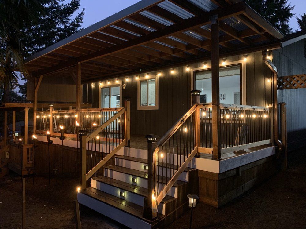 Cozy dark-colored home exterior with illuminated string lights on porch and stairs at dusk.