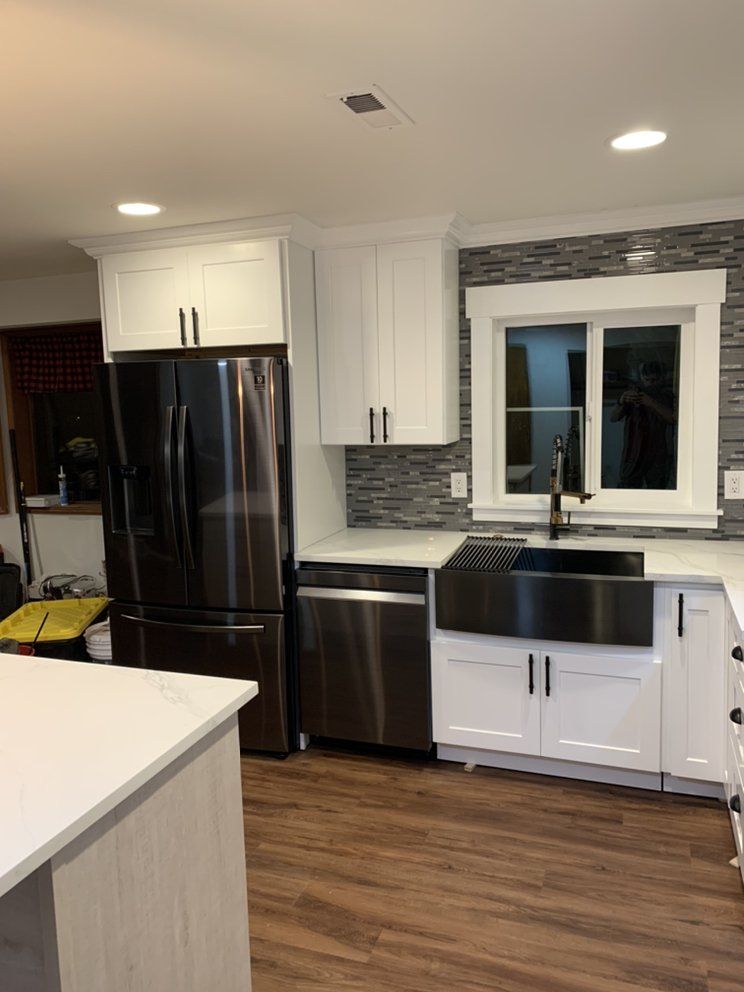 Modern kitchen with white cabinets, stainless steel appliances, dark sink, and wood-look flooring.