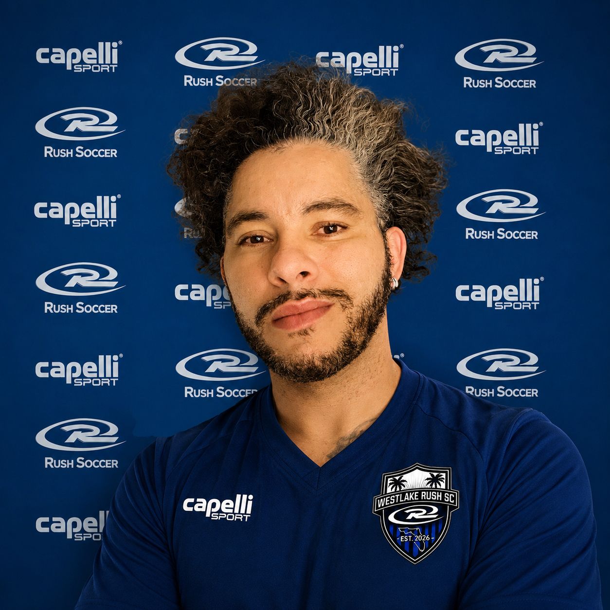 Portrait of a smiling person in a navy Capelli soccer jersey against a RSL Soccer logo backdrop