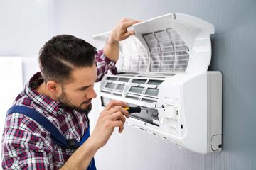 Happy Male Technician Repairing Air Conditioner With Screwdriver — St. George, UT — Peach Services LLC
