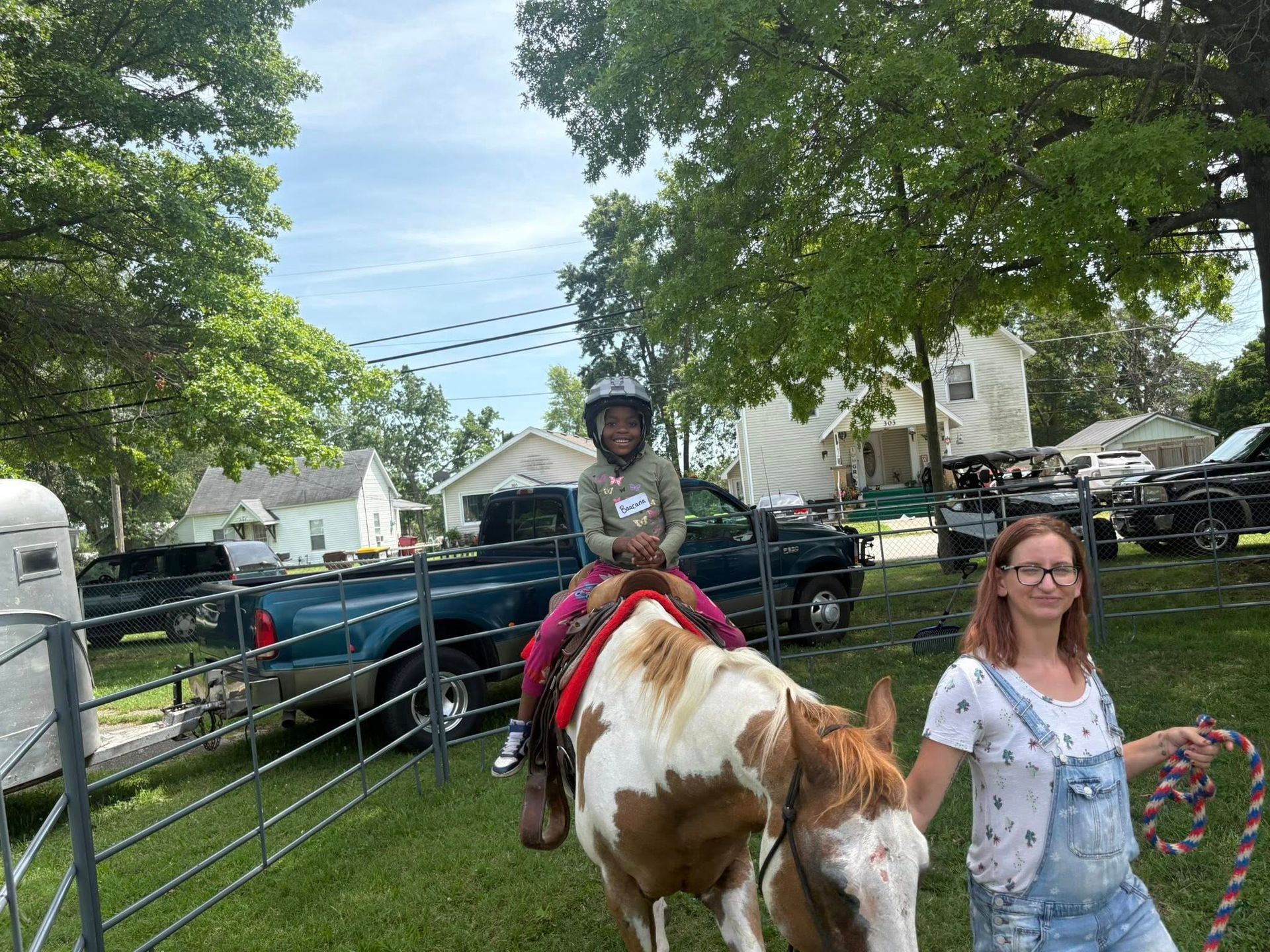 A woman is standing next to a child riding a horse.